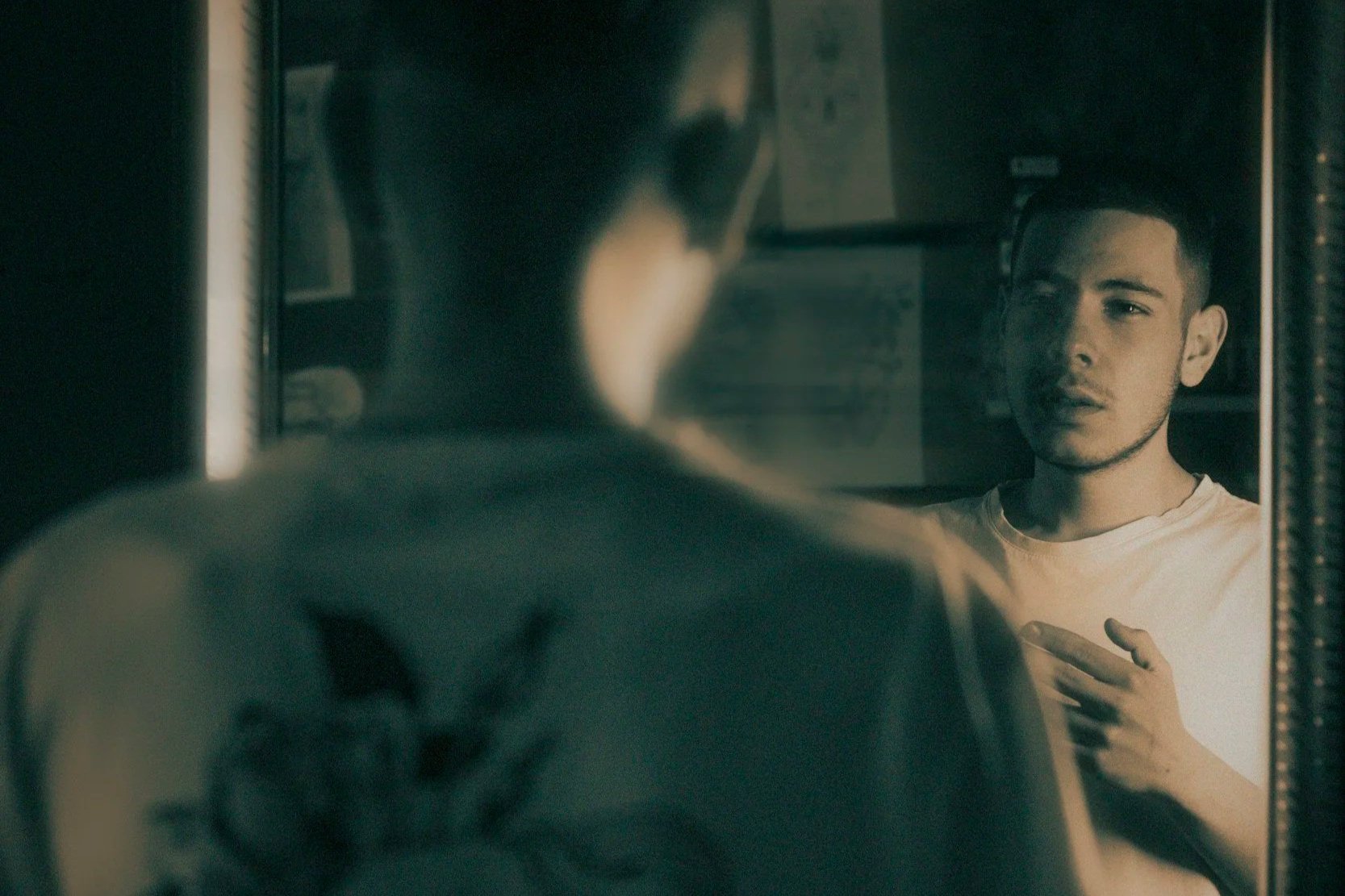 a photo of a man looking into a mirror with a serious expression on his face