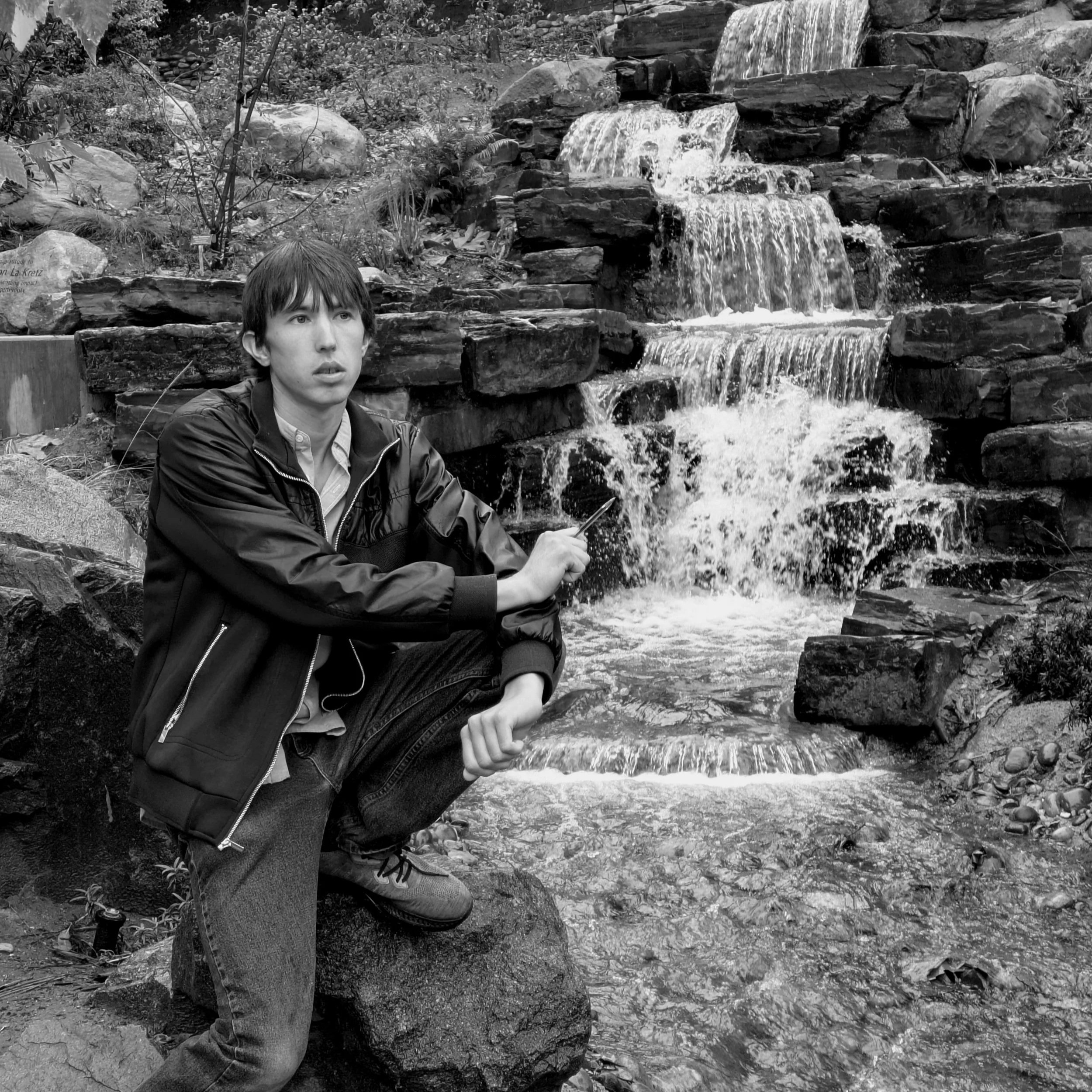 a black and white photo of sam hendrian sitting in front of a waterfall