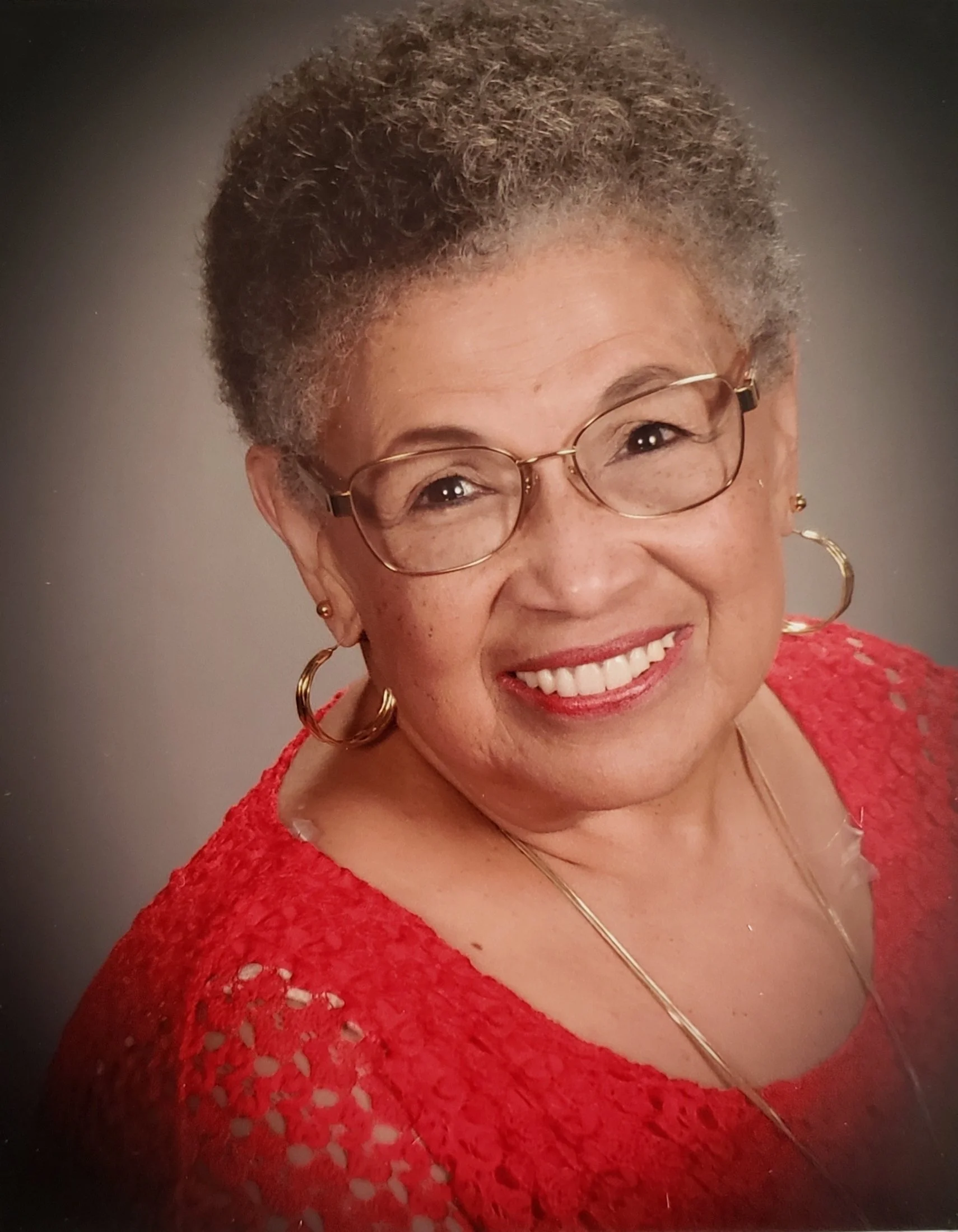 a headshot of andrea cummings wearing a red shirt on a gray background