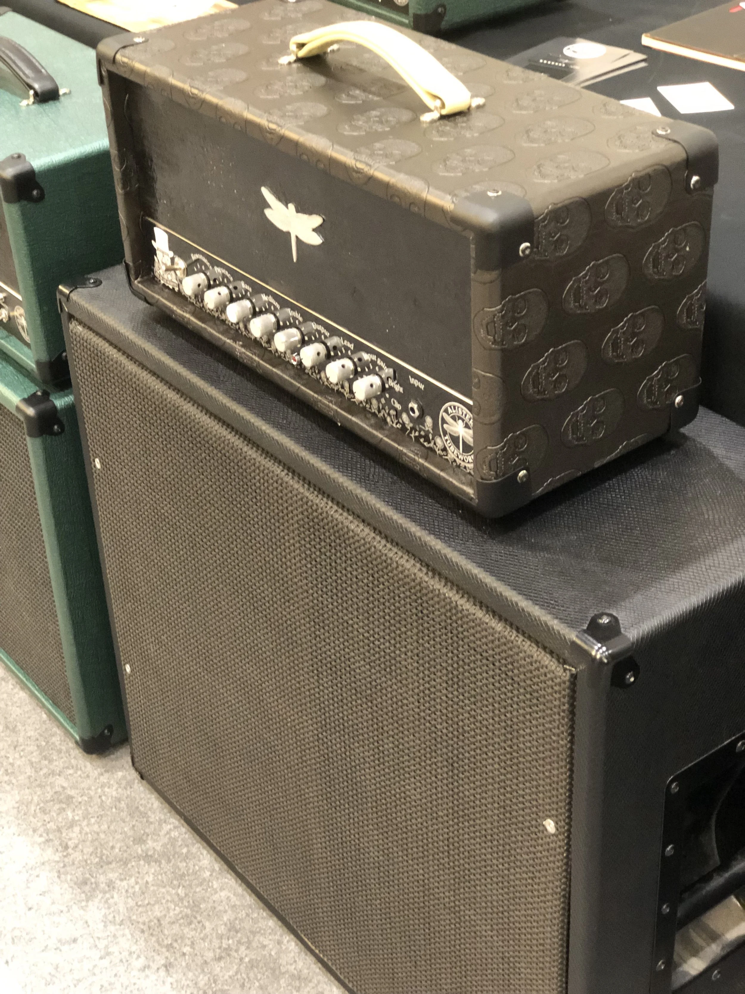 Une tête d'amplificateur de guitare noire avec un symbole de libellule blanche et des contrôles à boutons, posée sur un haut-parleur noir.