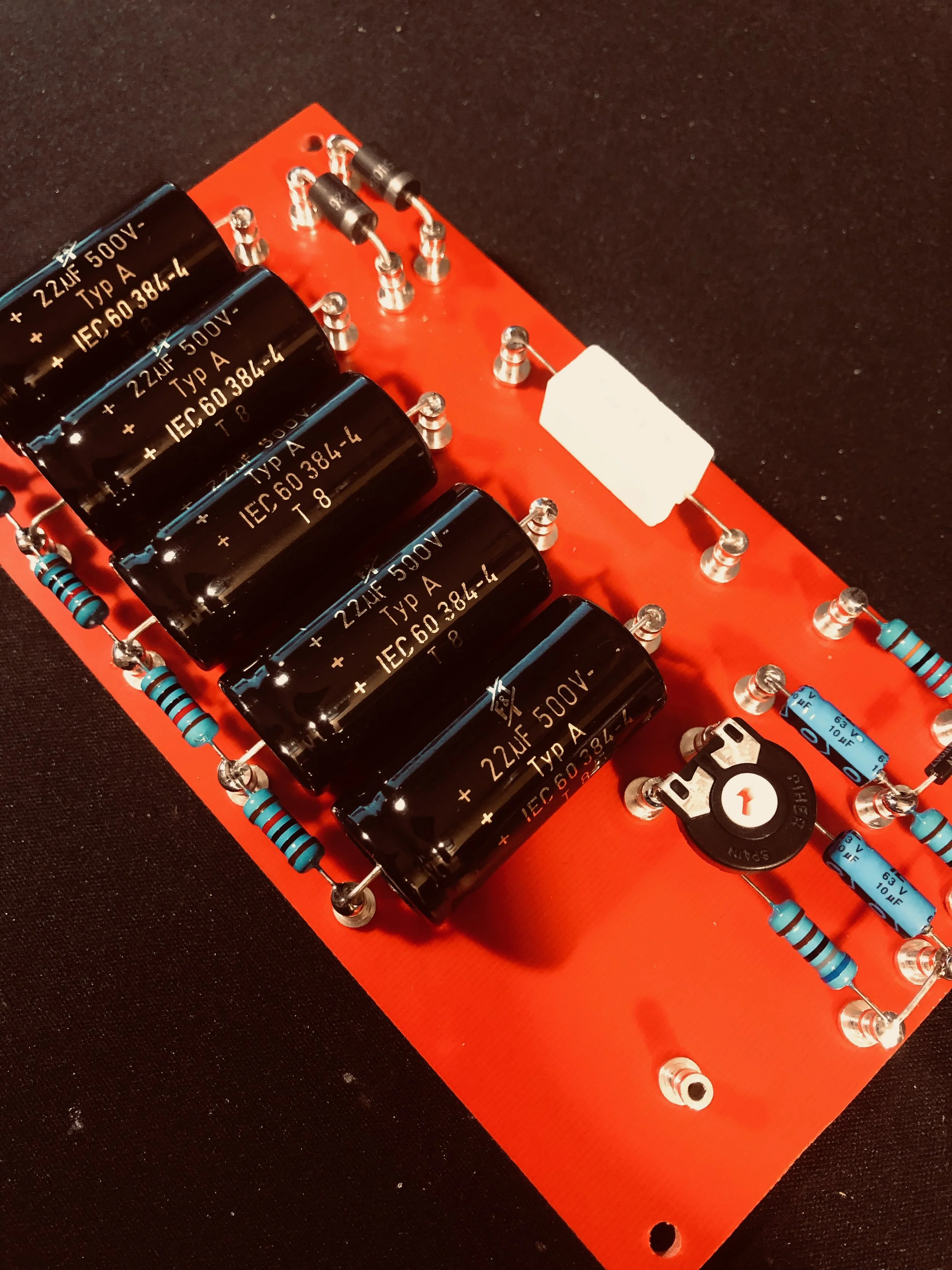 Carte électronique avec de grands condensateurs noirs, plusieurs résistances bleues, un commutateur rotatif et des composants en acier brillant, montée sur un circuit imprimé orange.