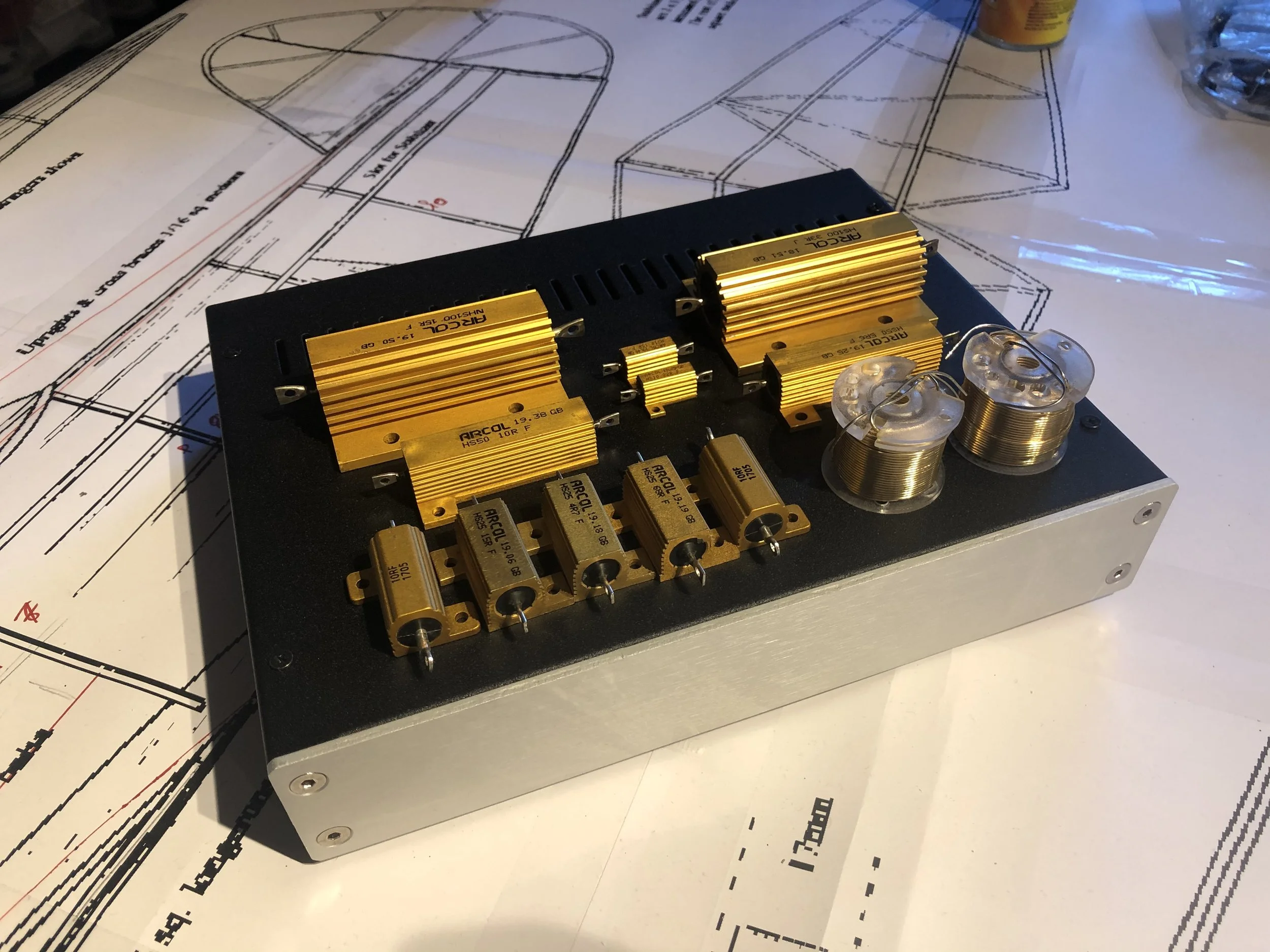 Un panneau électronique avec des dissipateurs en or, des condensateurs et des bobines, placé sur un plan de construction.