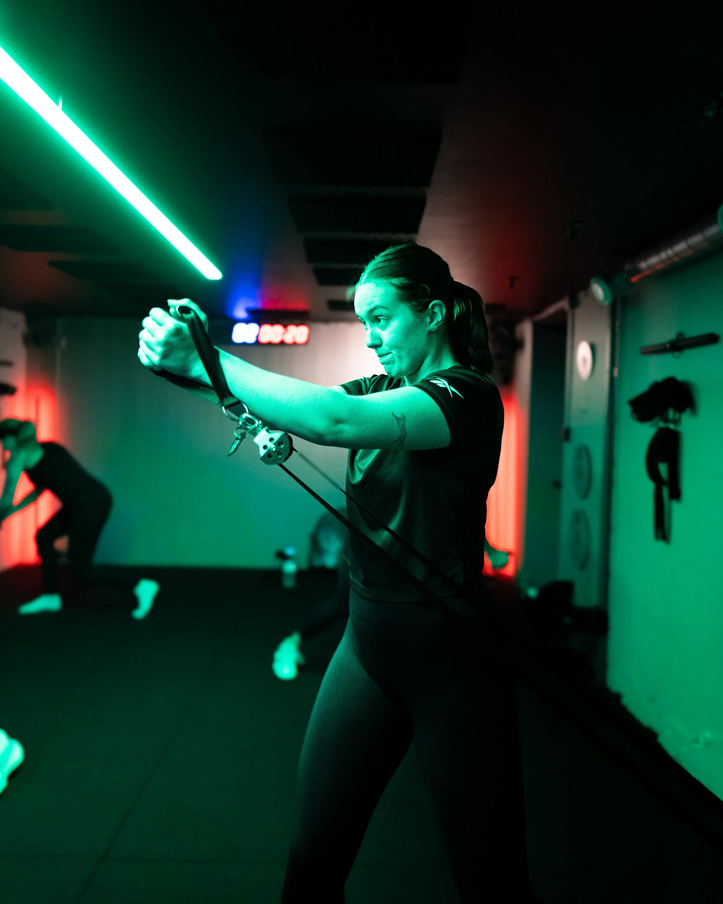 A woman exercises with a resistance band in a dimly lit gym with green and red lighting.