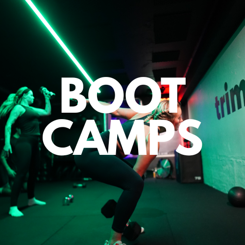 Group fitness class in a dark studio with colorful lights, featuring a woman performing an exercise and the text "BOOT CAMPS" overlayed.