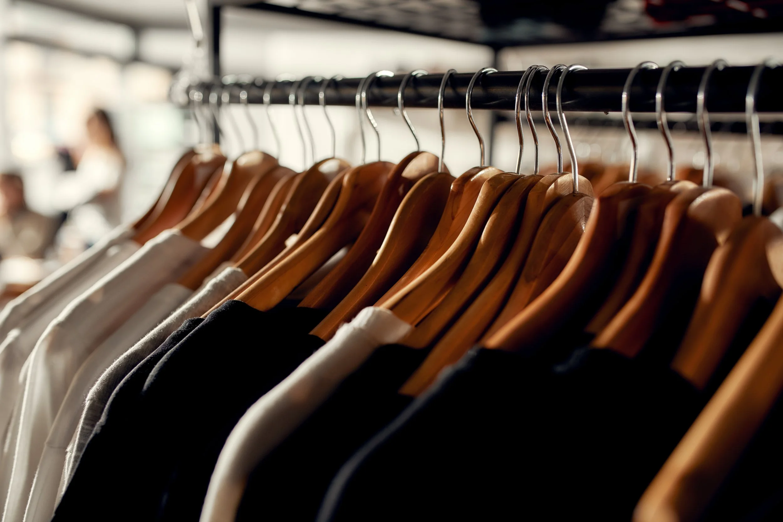 Hangers with clothing hanging on a metal rod inside a closet or clothing store.