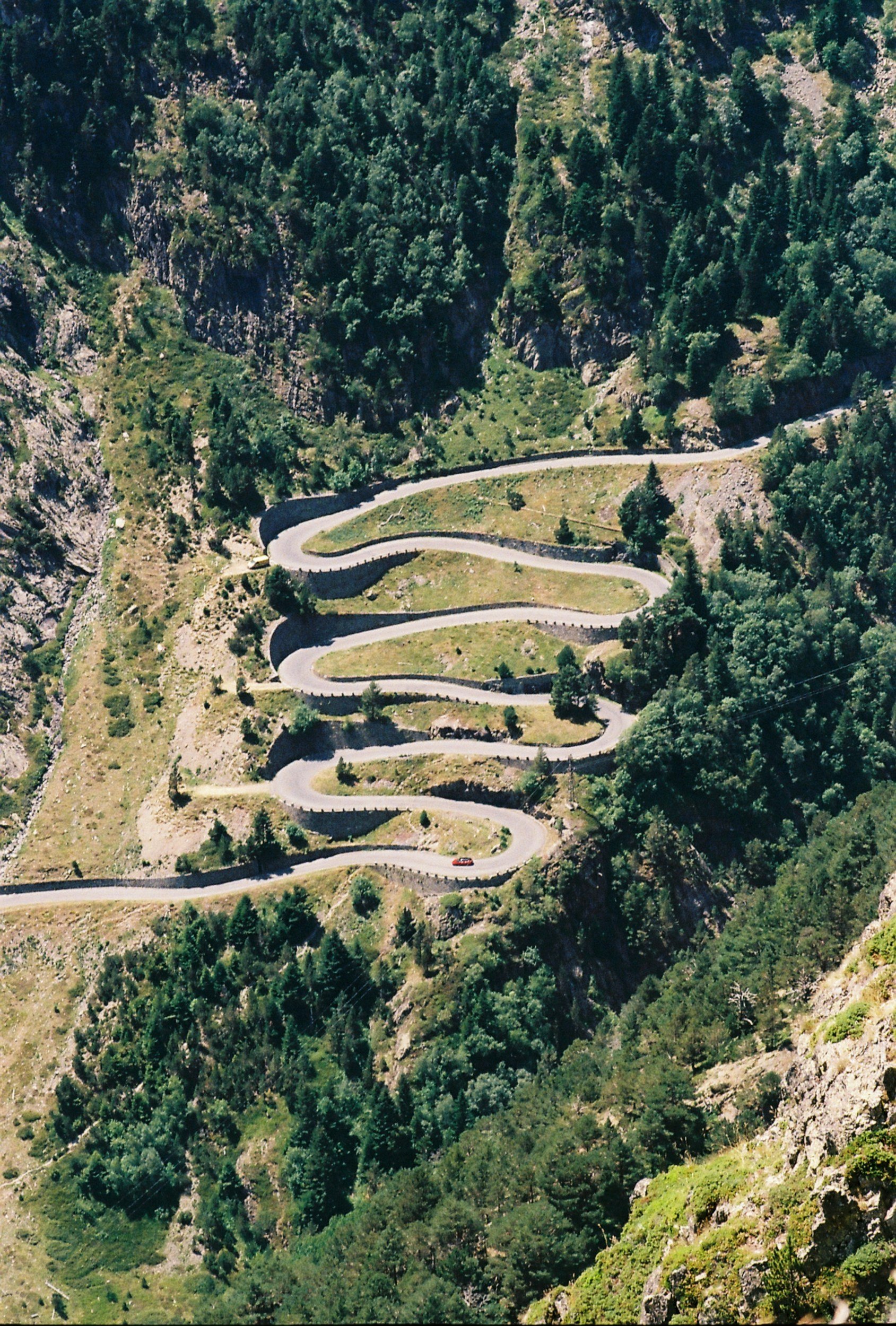 A winding mountain road with multiple sharp turns, surrounded by lush green trees and rocky cliffs.