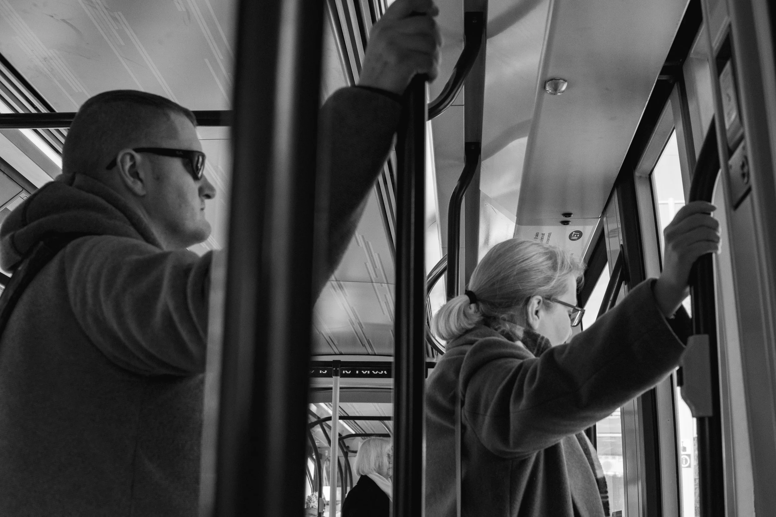 Two passengers holding onto handrails inside a bus, looking out the windows, black and white photo.