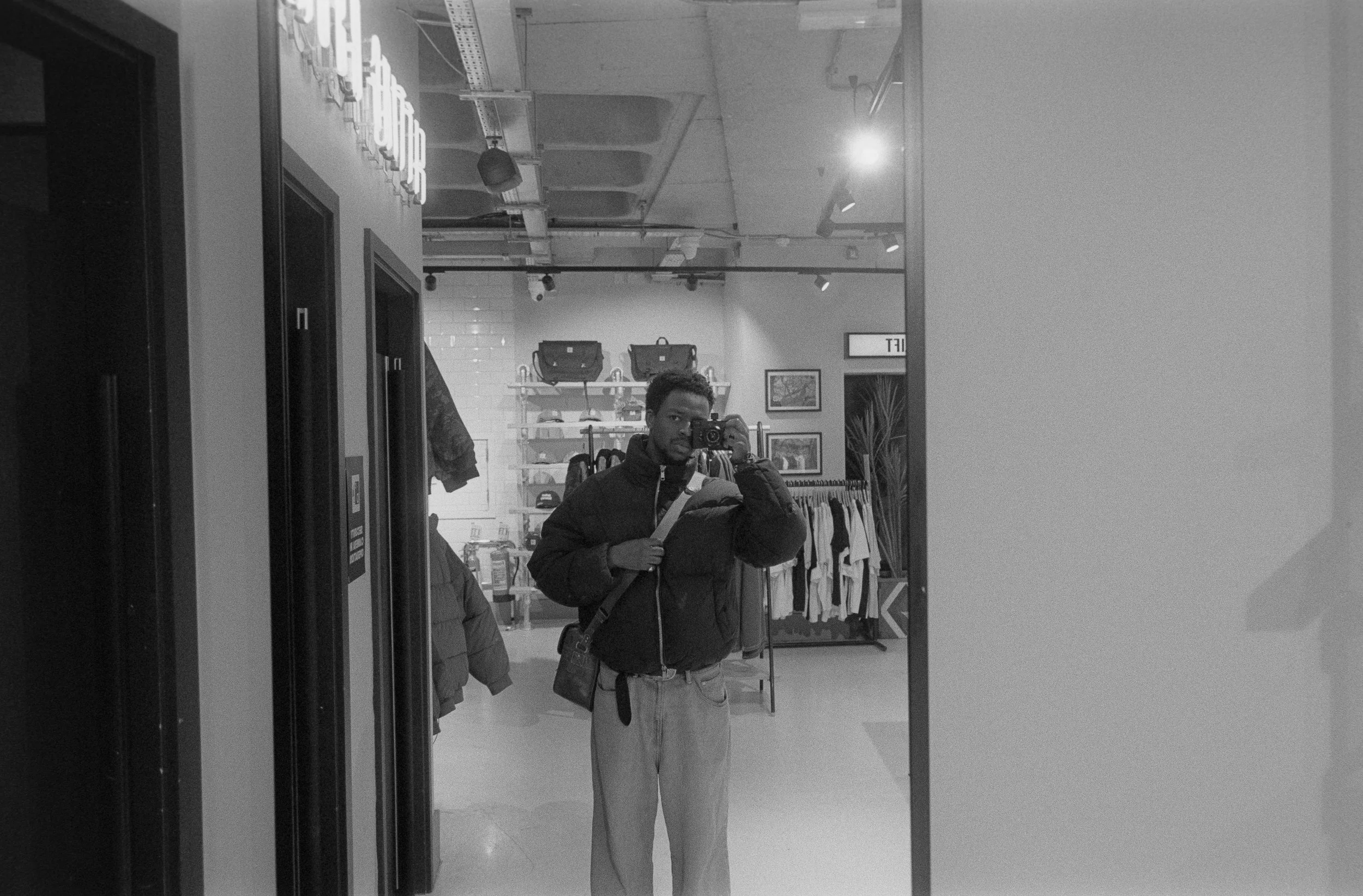 A person taking a selfie in a store mirror, surrounded by racks of clothing and handbags.