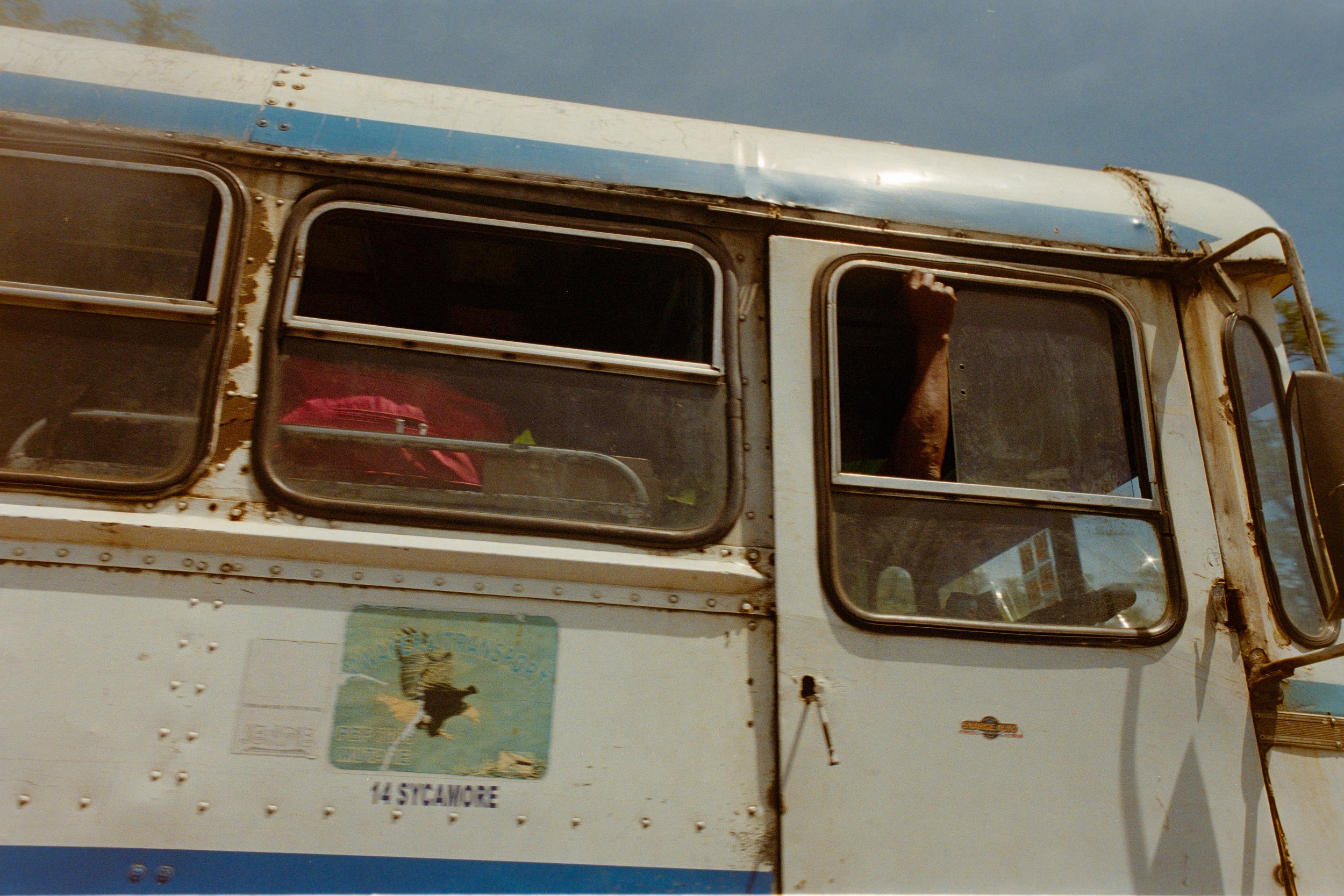 Close-up of an old bus with scratched windows, rust, and a raised fist of a person visible through the open window.