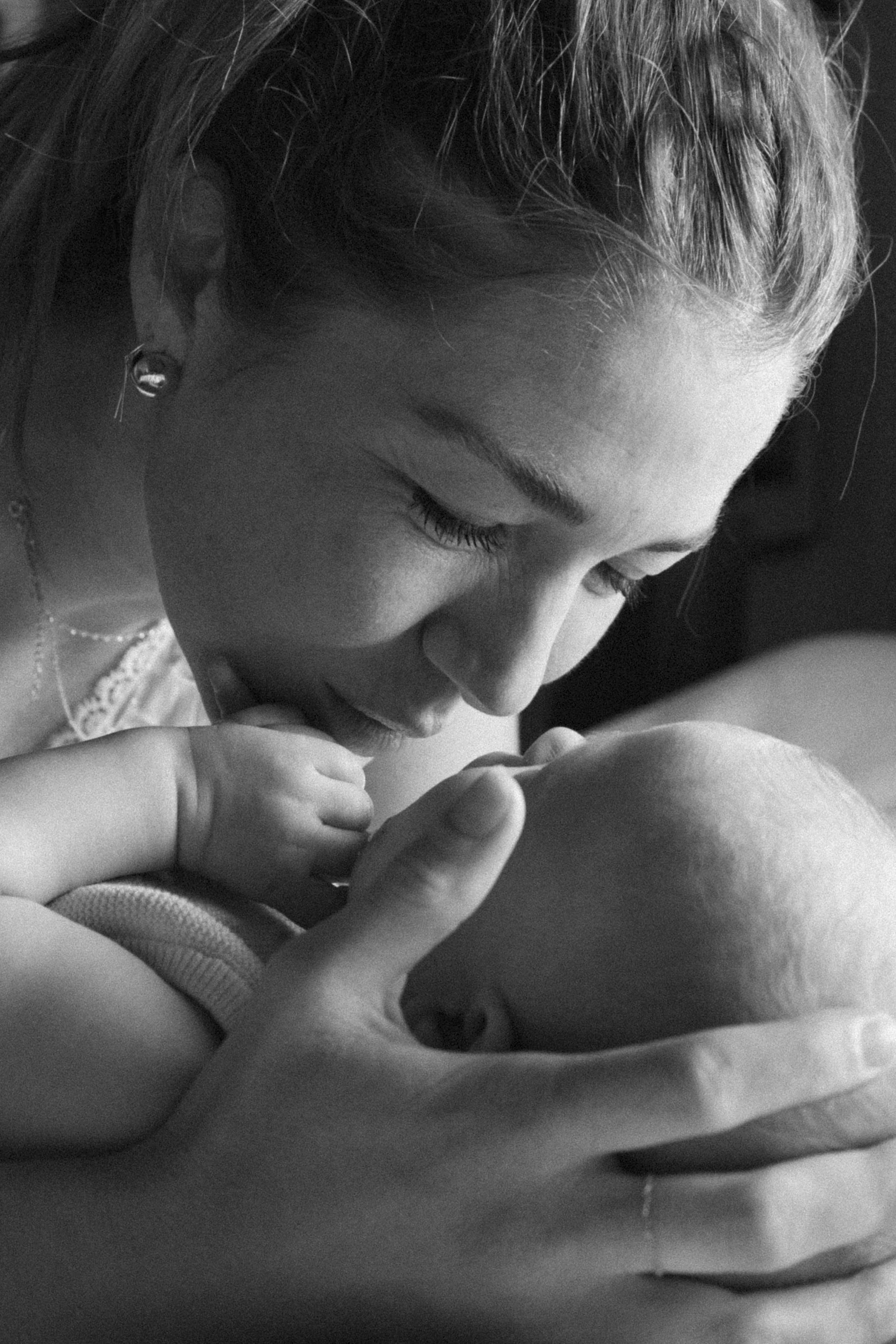 A woman gently kissing a baby on the forehead, both with closed eyes, in a black-and-white photograph.