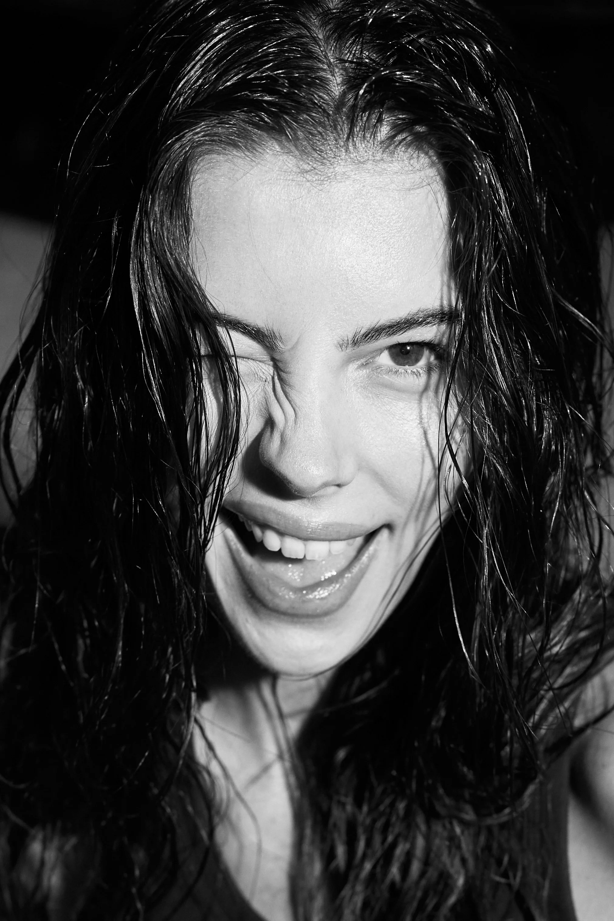 A woman with wet hair winking and smiling, in a close-up black and white portrait.