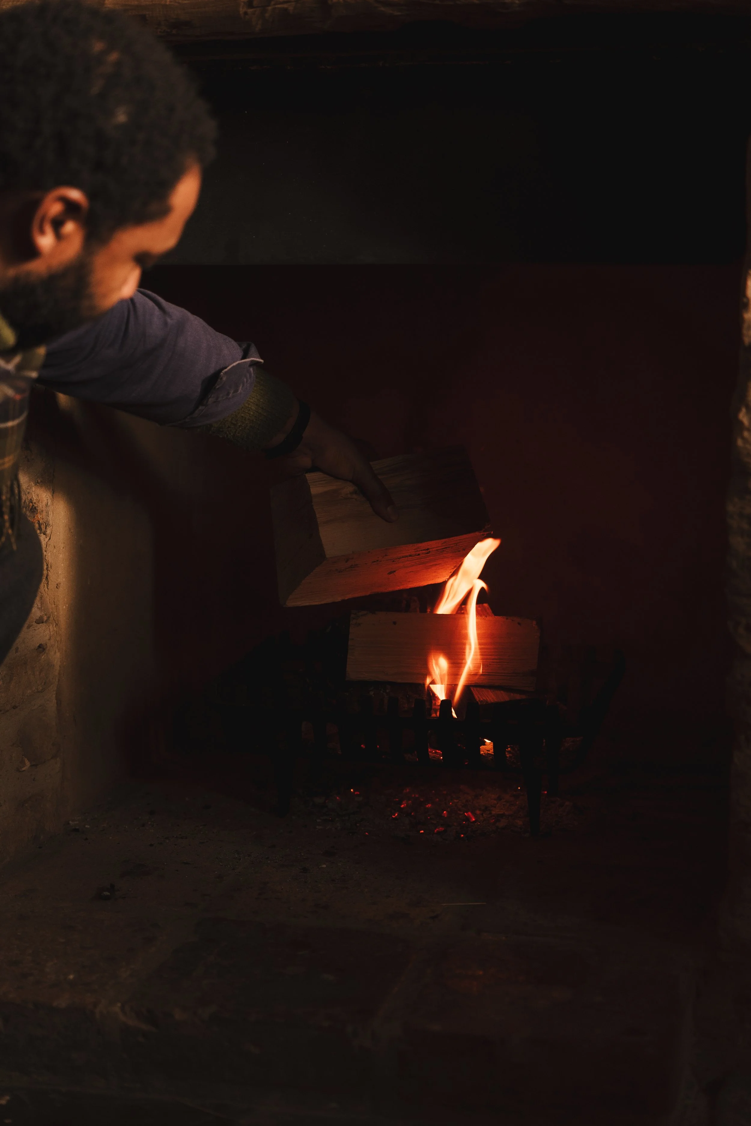 A person stacking firewood in a fireplace with a small fire burning.