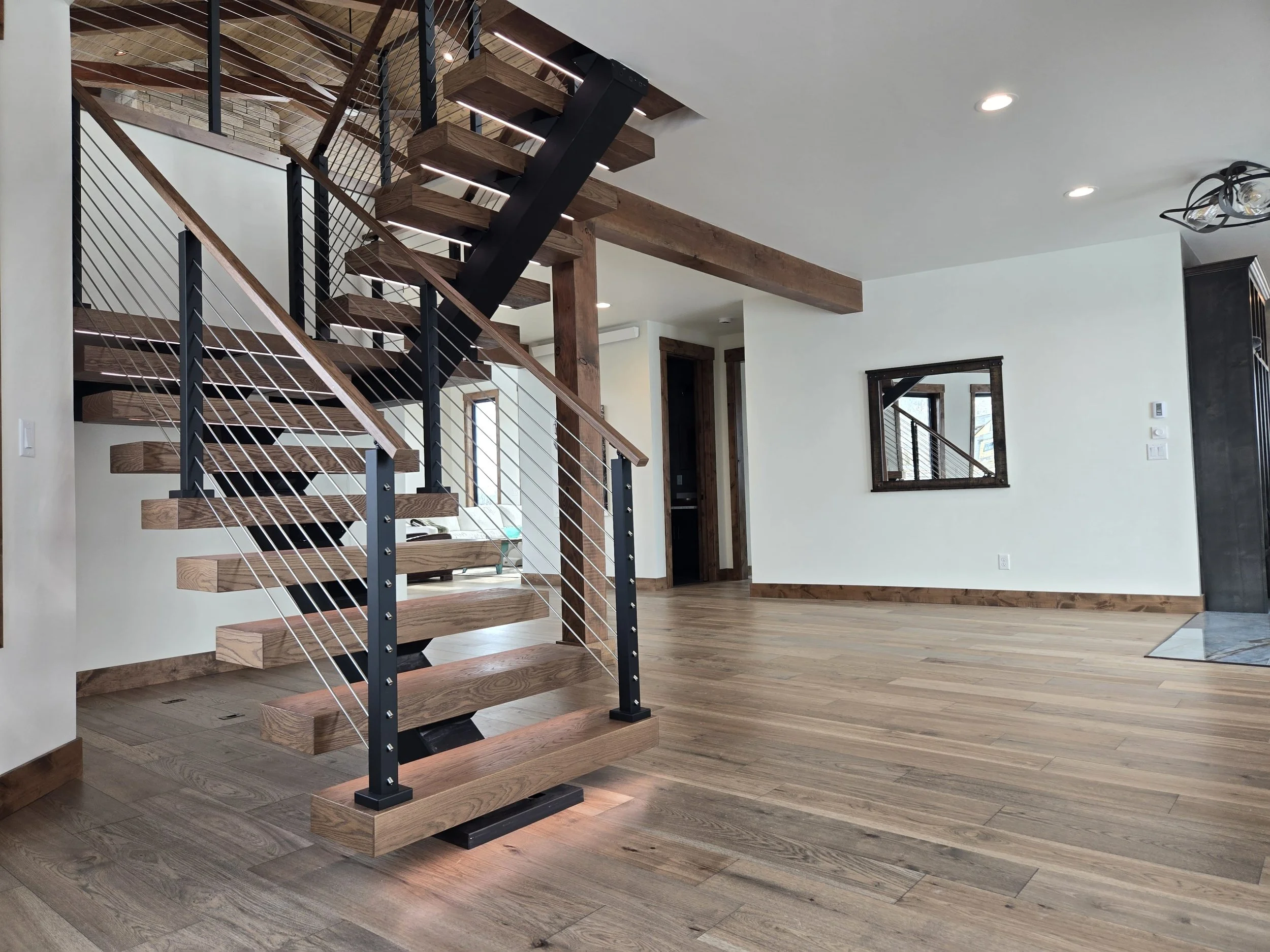 Modern living room with wooden floors, a staircase with wooden steps and black metal railings, and a wall mirror.