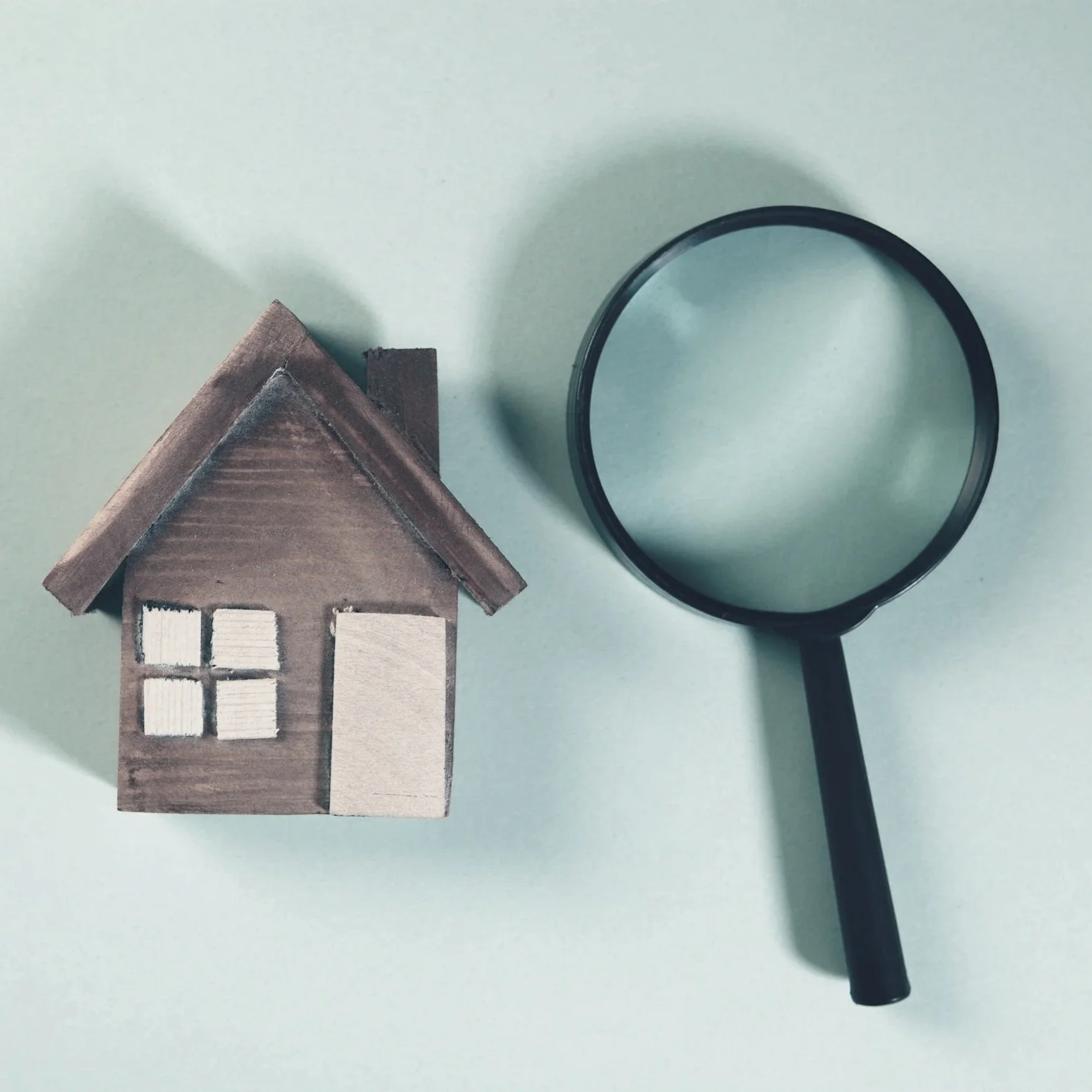 A small model home next to a magnifying glass representing inspections (such as code, and structural inspections) that need to take place before a home or buiilding is occupied.
