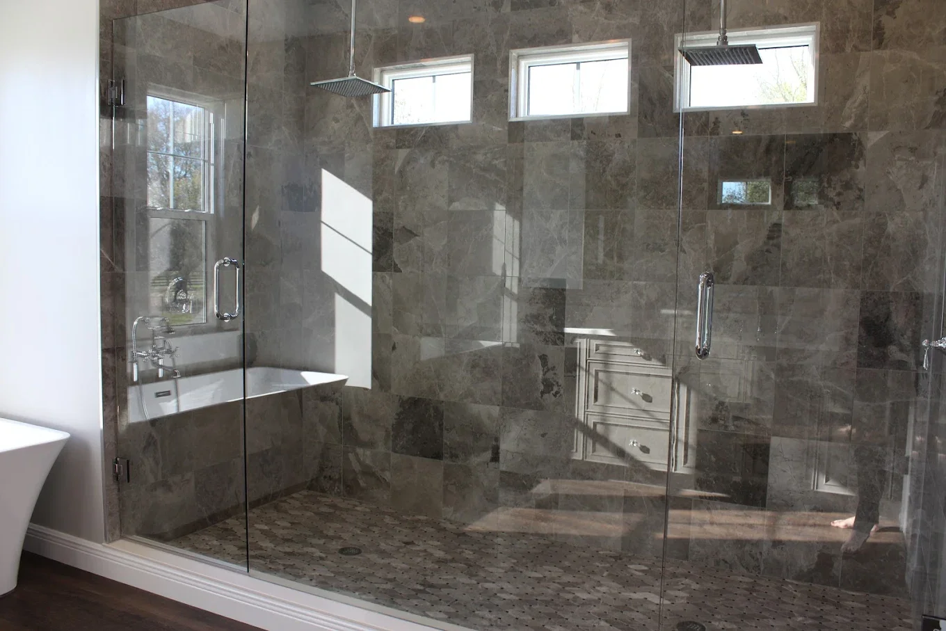 A modern walk-in shower with glass doors, gray marble tiles on the walls, small window panes, and a rainfall showerhead on the ceiling.