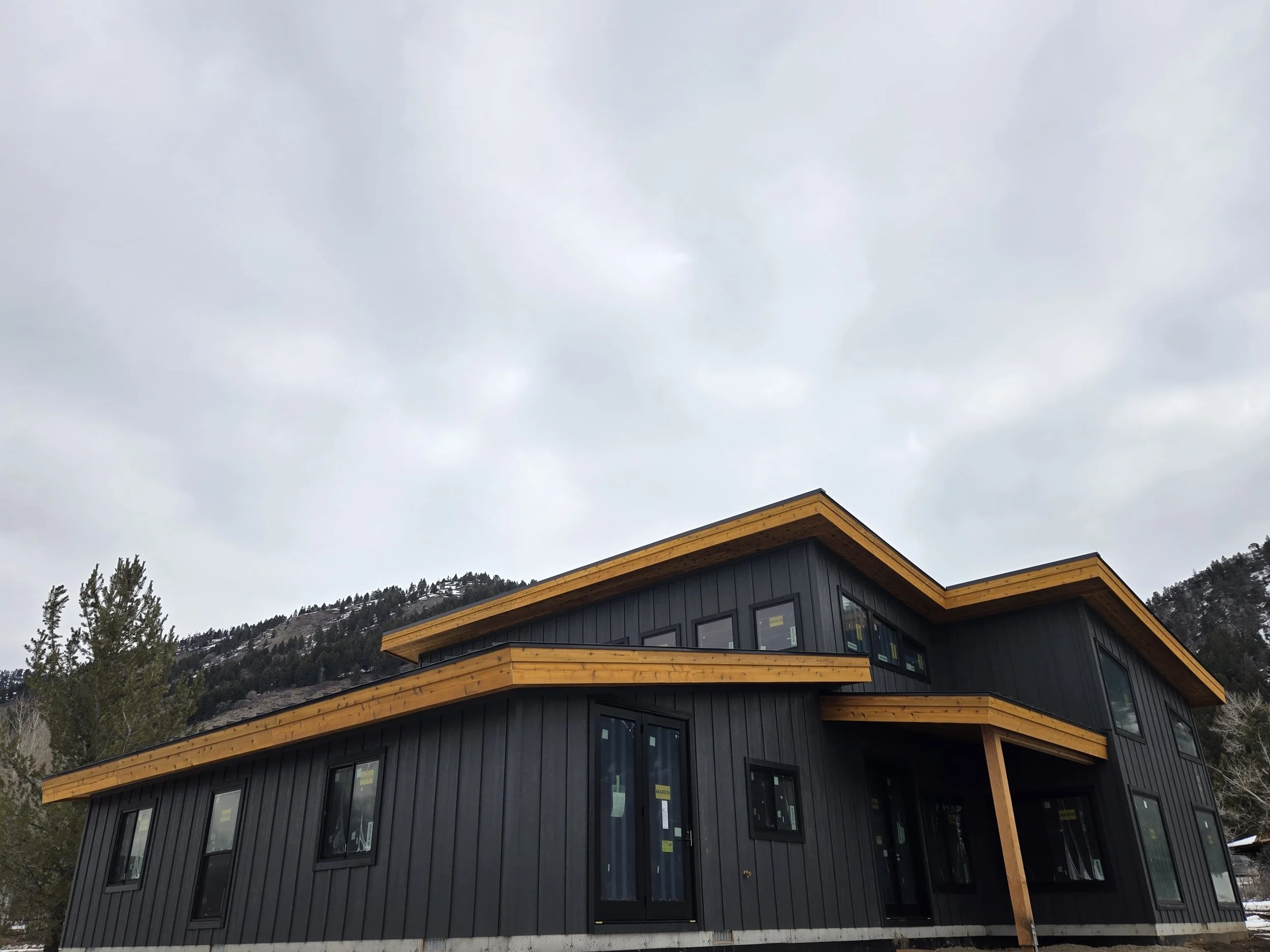 Exterior view of a modern rustic style home located in Alpine, Wyoming. Heavy timber accents with a batt & board style black siding.
