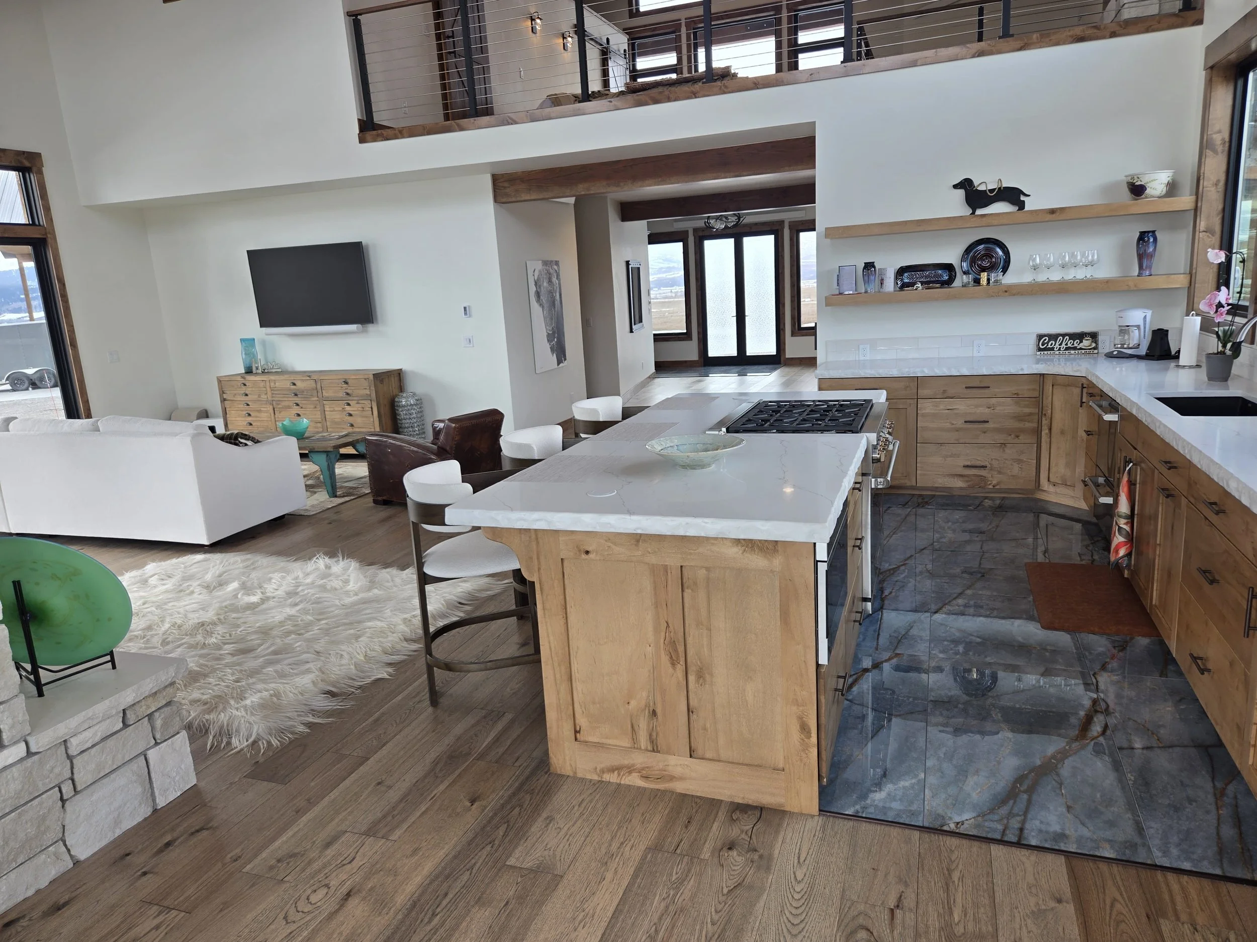 Open-concept kitchen and living room with wooden accents, a white sofa, a TV, and decorative items on shelves.