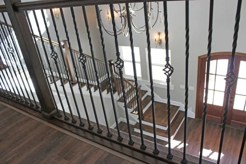 View of a staircase with wooden steps and a black iron railing from an upstairs vantage point, featuring a wooden door with glass panels to the right.