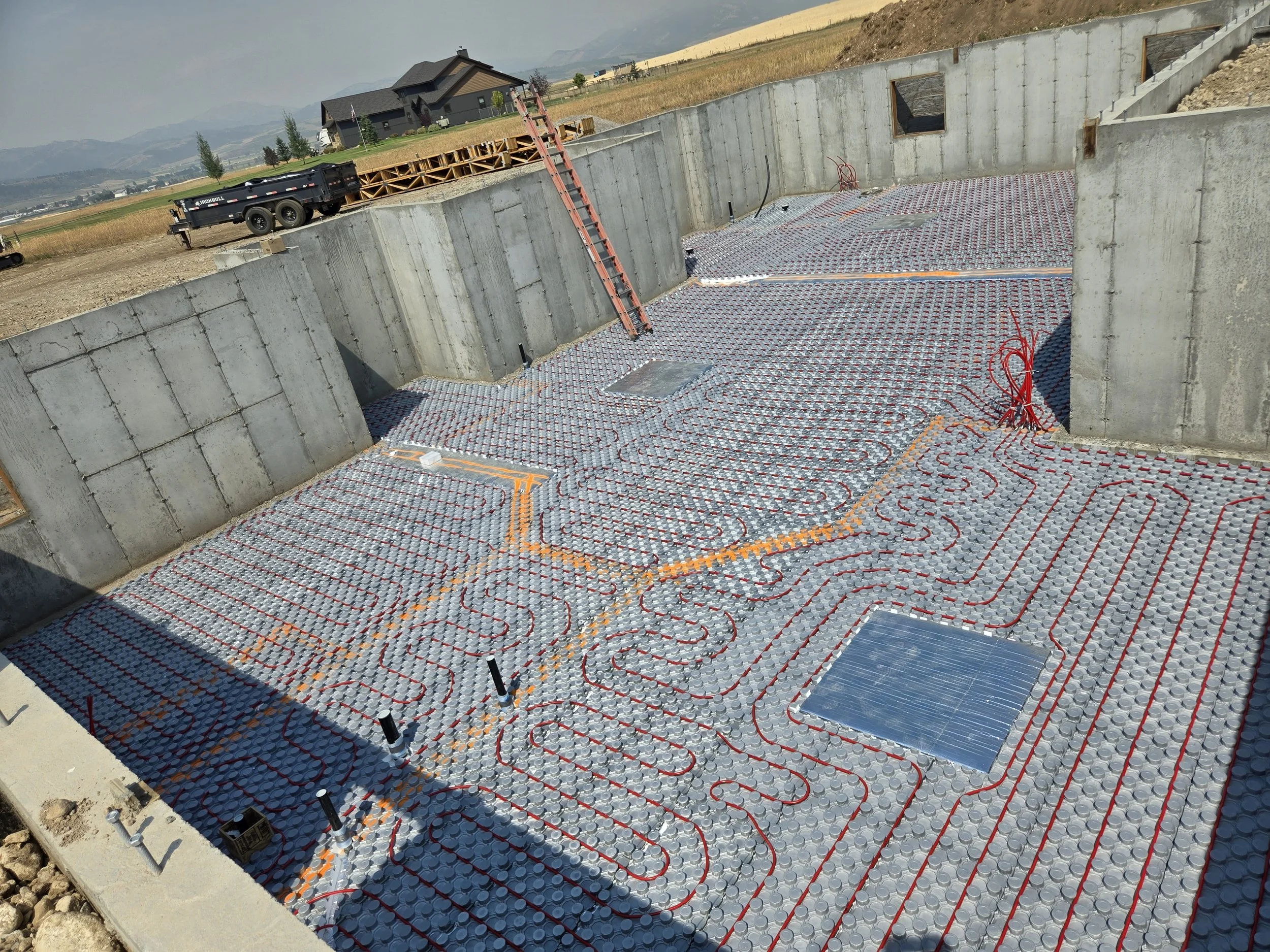 Construction site with a concrete foundation and underfloor radiant heating system installed with red PEX tubing and insulation panels.