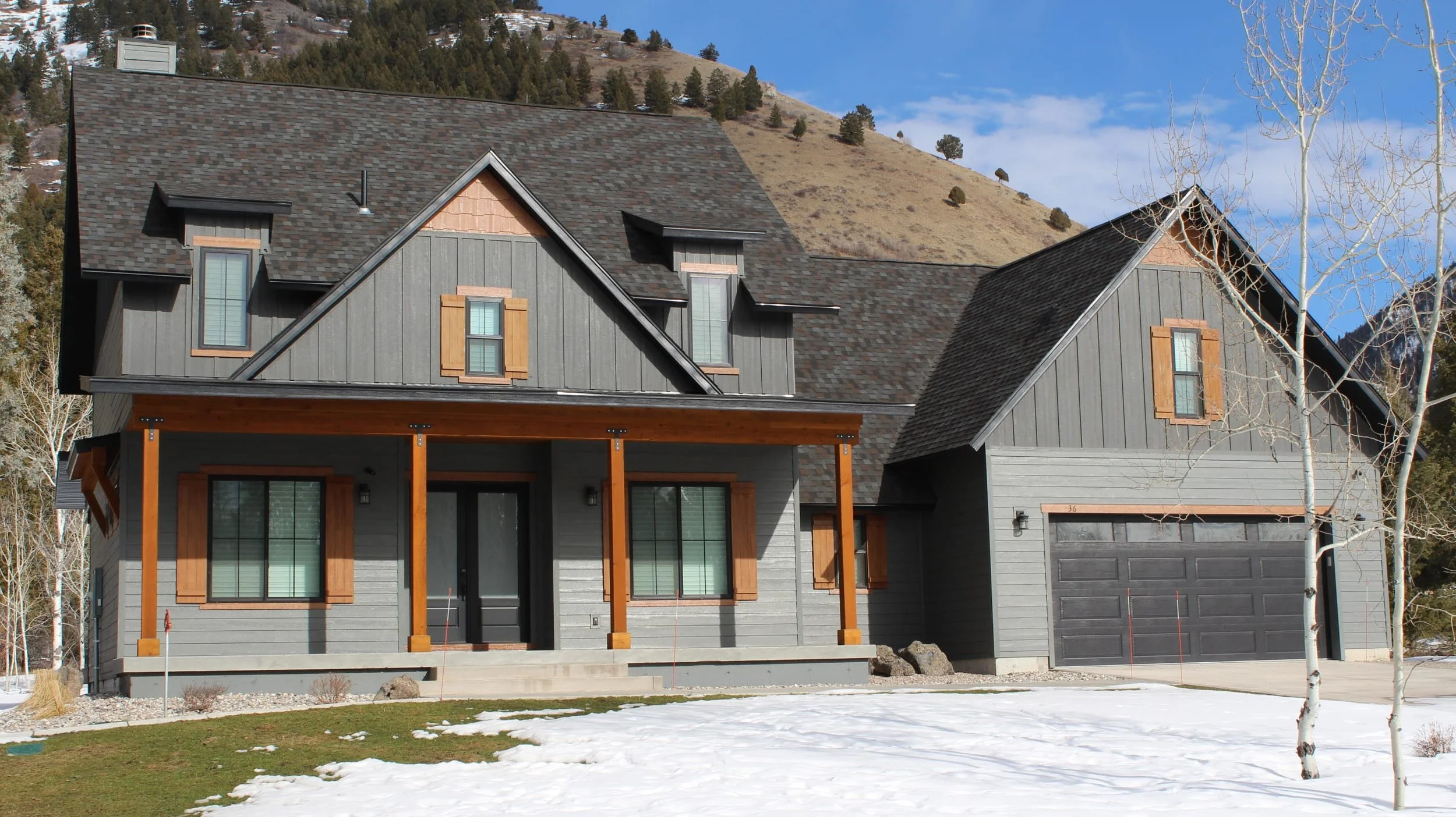 Custom home built in Alpine Wyoming. Dark grey siding with timber accents and shutters. Mountain in the background.