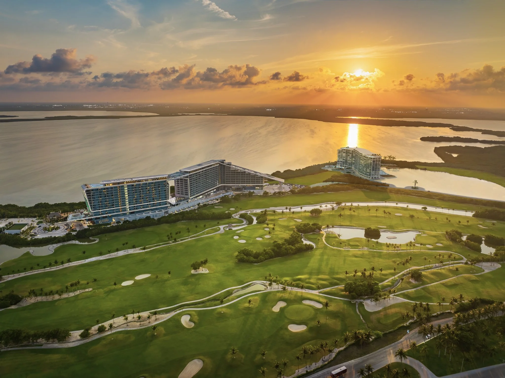 Sunset over a golf course and waterfront with modern buildings in the background.