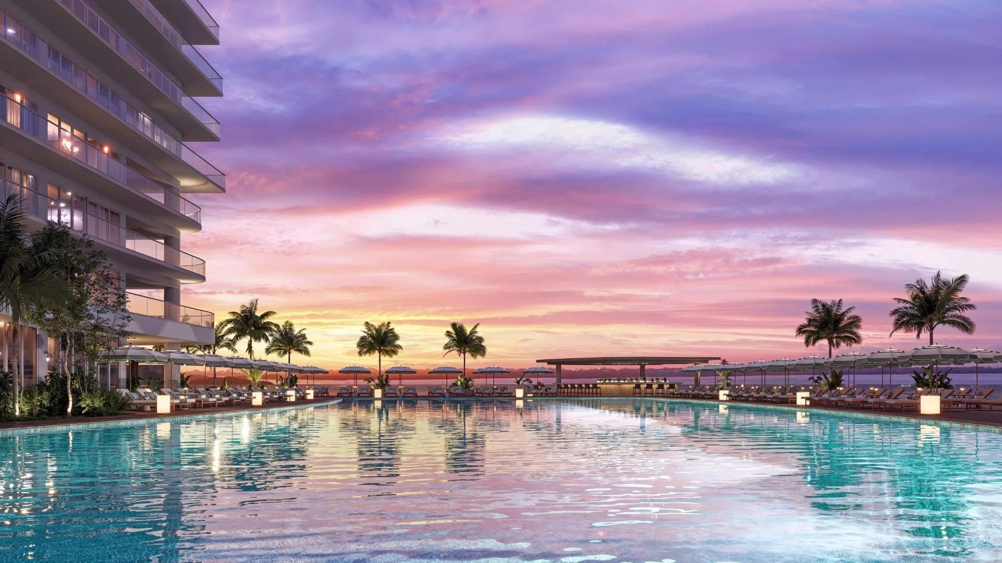 A luxurious outdoor swimming pool area at sunset, surrounded by palm trees, lounge chairs with umbrellas, and a modern building with balconies on the left.