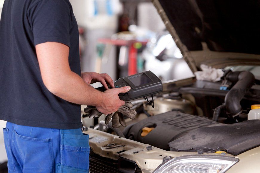 Auto mechanic inspecting a car engine with diagnostic equipment in a garage.