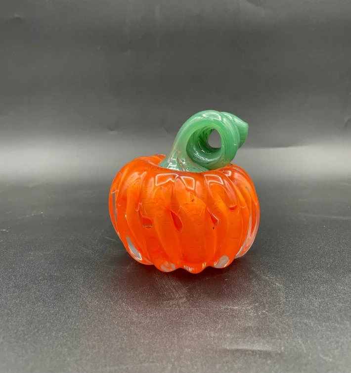 Glass pumpkin with a bright orange body and a green swirl stem on a dark surface.