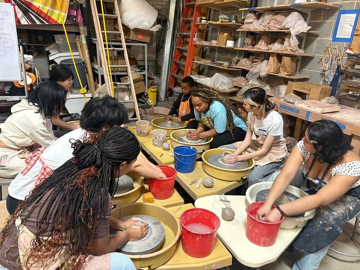 Group of people participating in a pottery class, working on clay wheels in a workshop