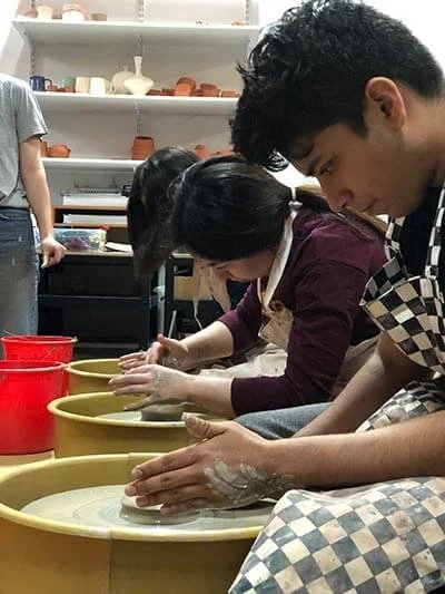 People participating in a pottery class, shaping clay on pottery wheels in a studio.