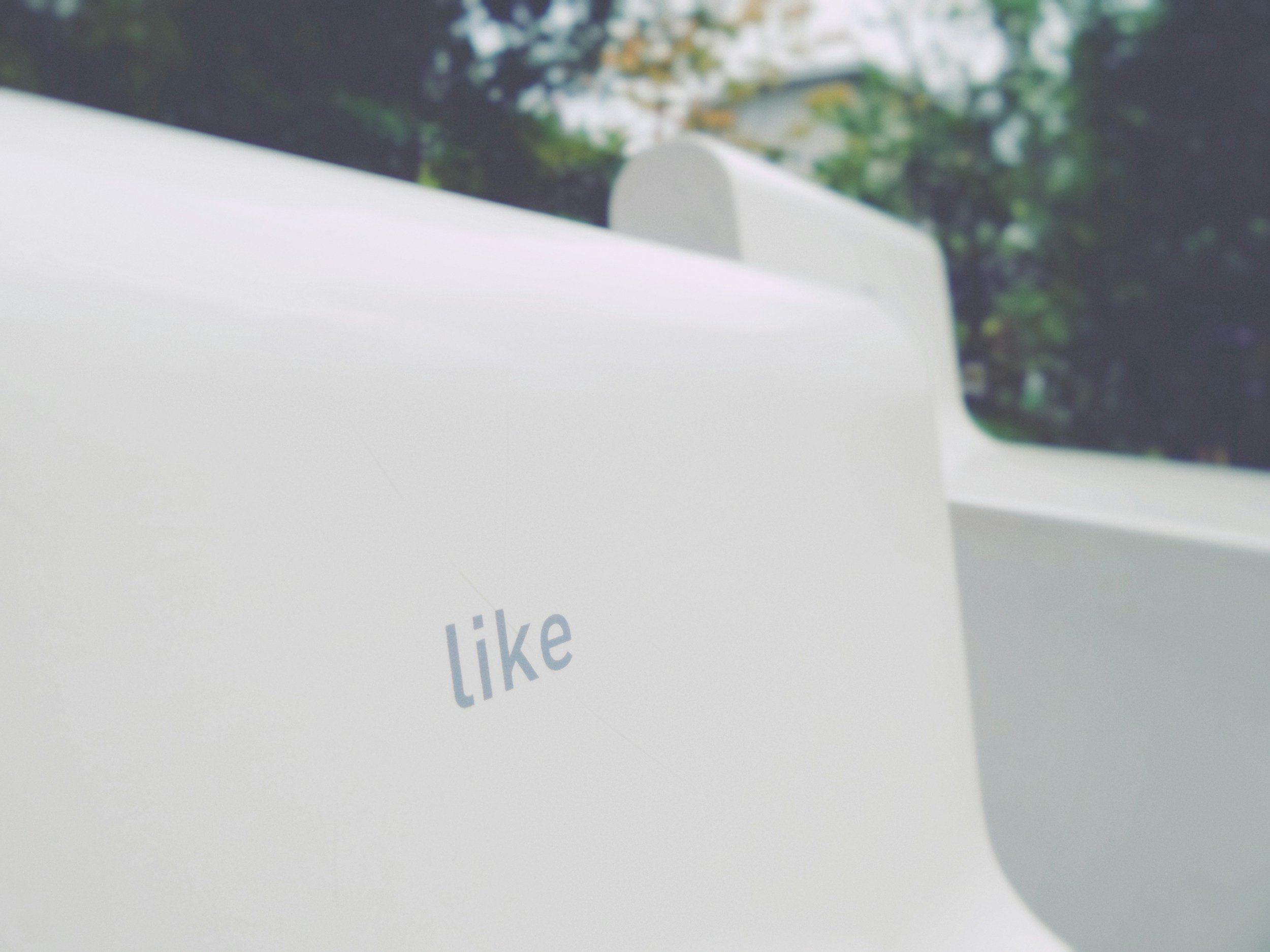 Close-up of a white object with the word 'like' printed on it, with a background of trees and sky, outdoors.