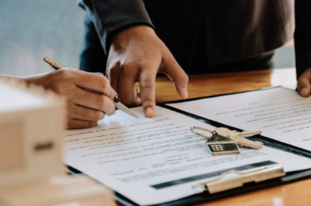 Person signing documents on a desk with keys and a house-shaped keychain, highlighting an agreement or contract.