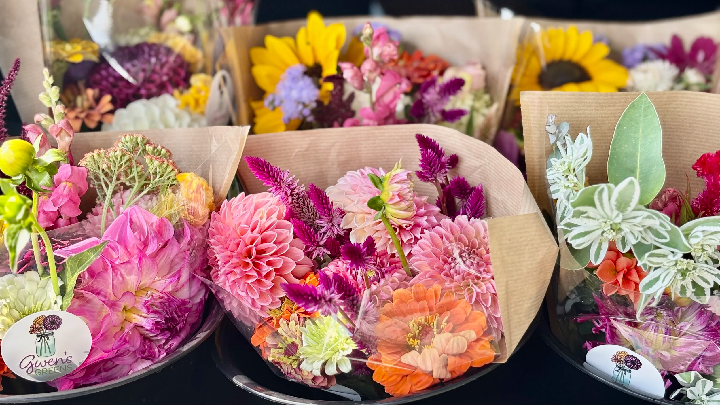 Various colorful flower bouquets wrapped in brown paper with a Gwen's Greens sticker on some.