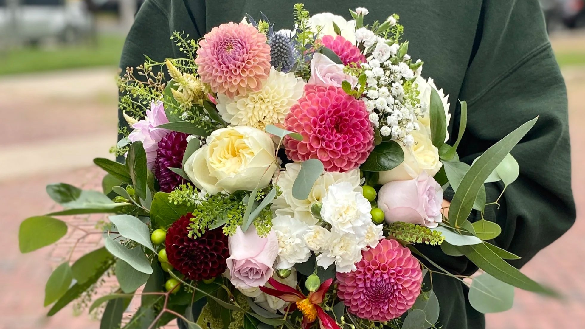 Person holding a colorful bouquet of flowers, including dahlias, roses, baby's breath, and greenery.