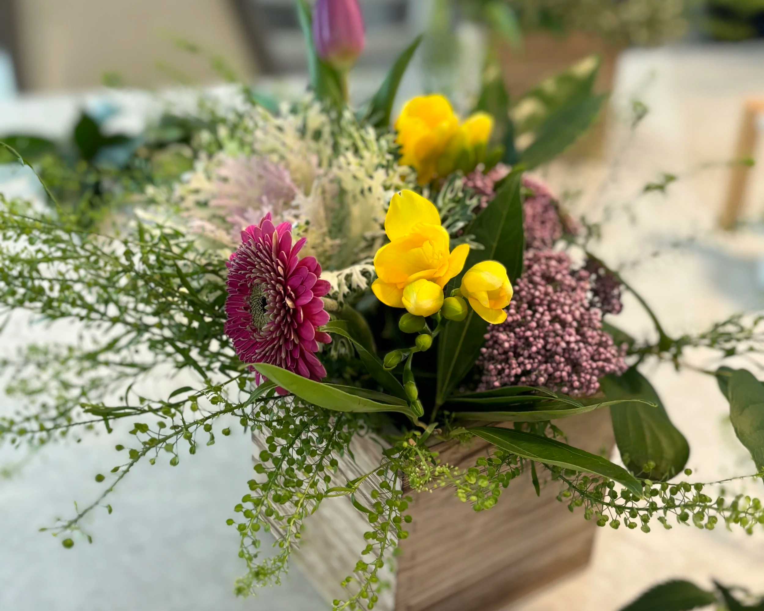 Close-up of a table bouquet with pink, yellow, white, and purple flowers, green leaves, and small green berries.