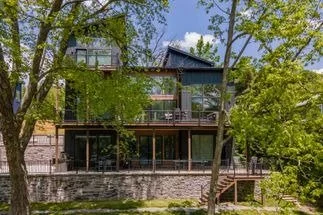 Modern house with large glass windows, surrounded by trees and greenery