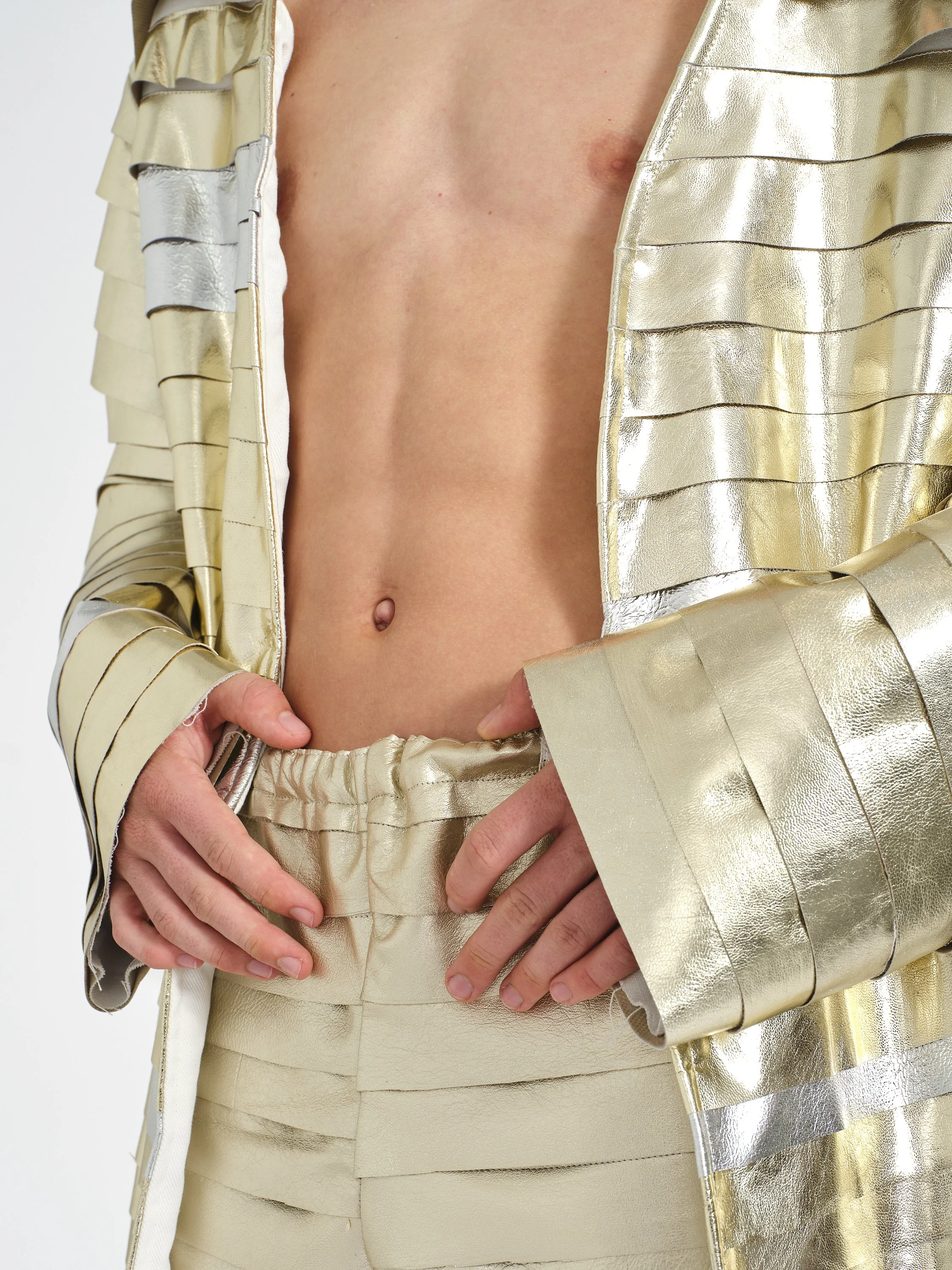 Close-up of a pregnant person’s bare belly framed by hands and a shimmering gold maternity outfit