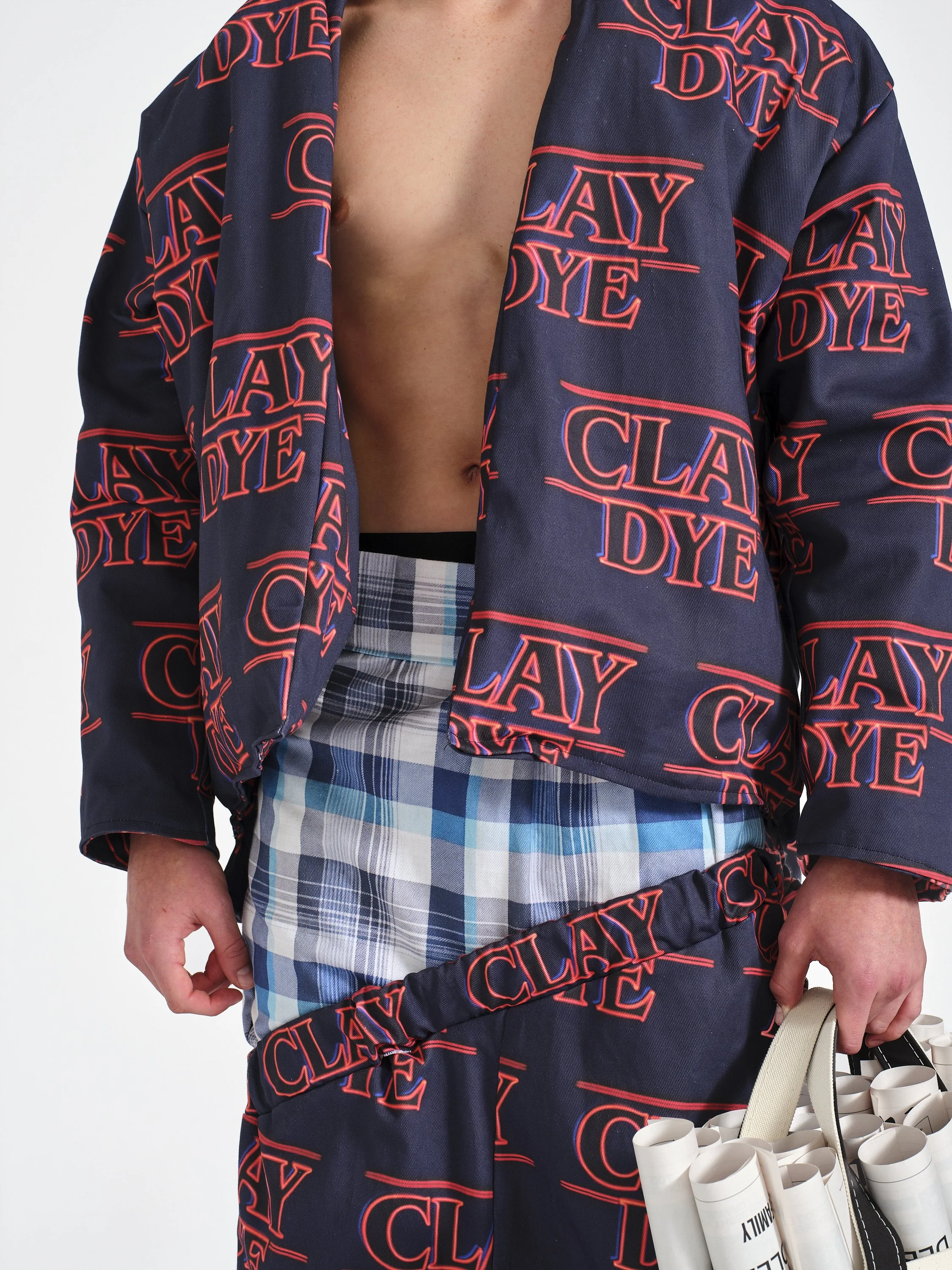 Person wearing a navy printed jacket over a blue plaid shirt and carrying a white canvas tote bag