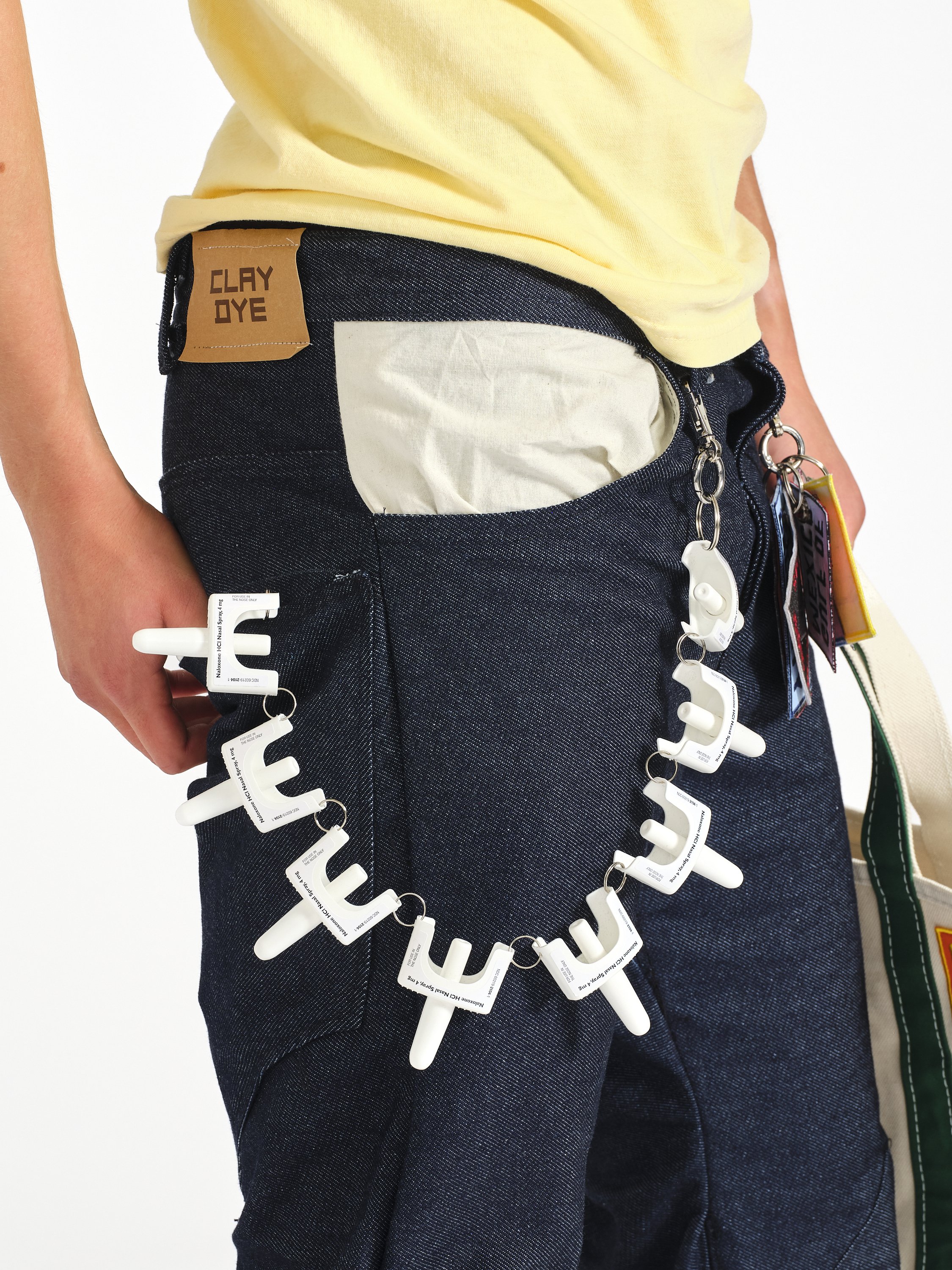 Close-up of a person wearing a navy denim utility apron with multiple naloxone nasal spray devices clipped to it.