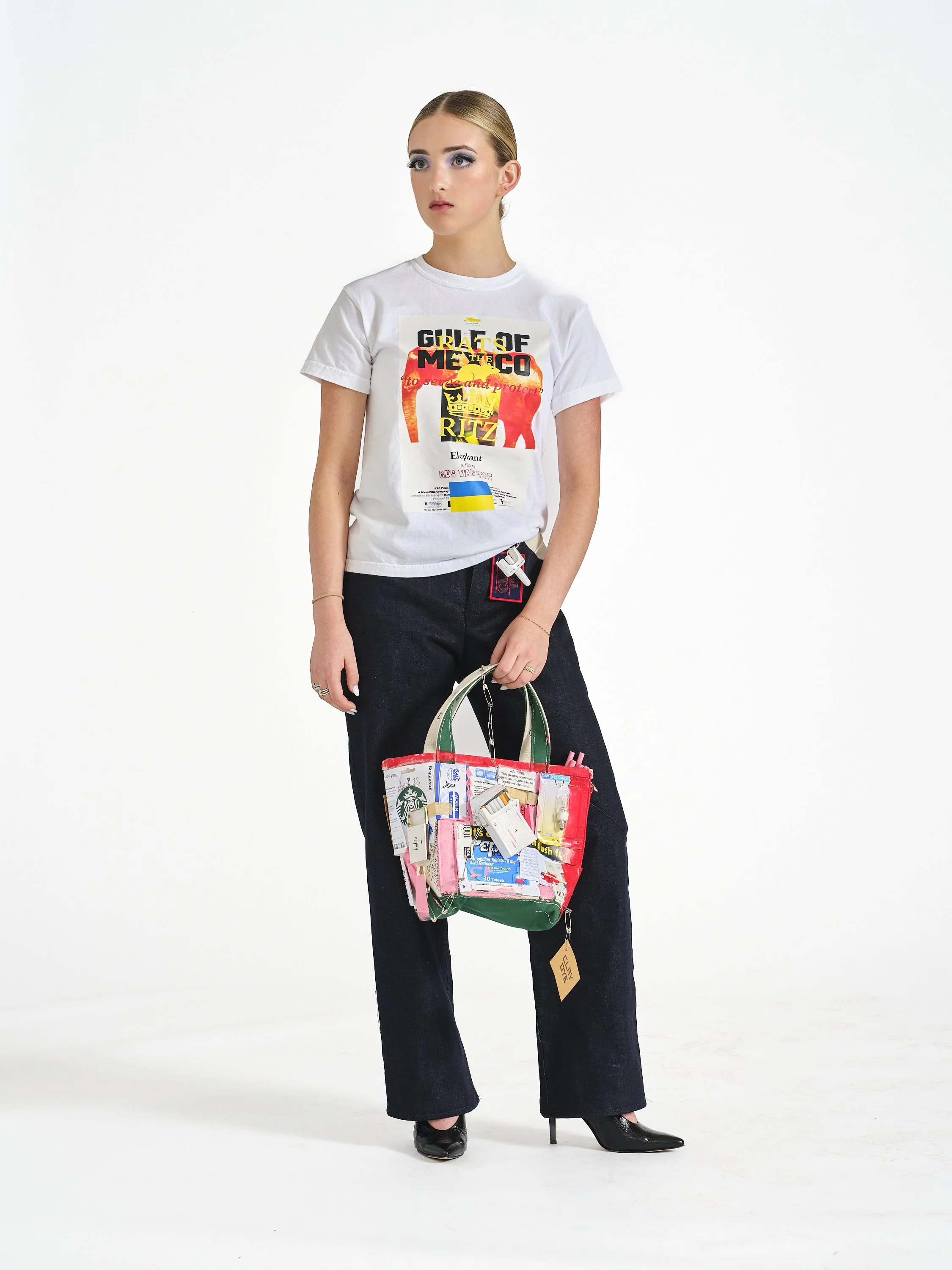 Female model stands posed in Clay Dye denim holding a custom small tote bag.