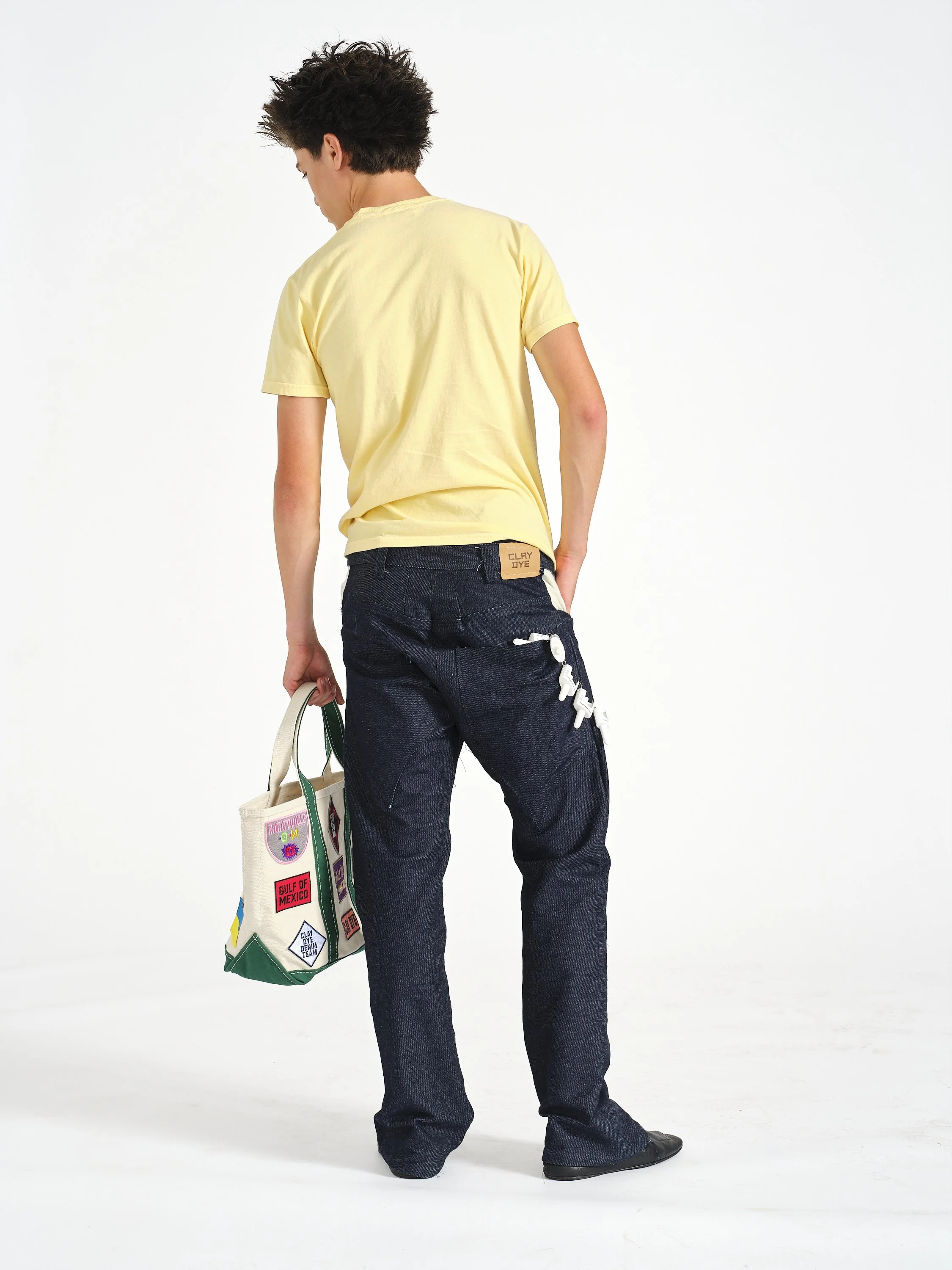 Back view of a person wearing a yellow T-shirt and dark wide-leg jeans, carrying a colorful canvas tote bag.