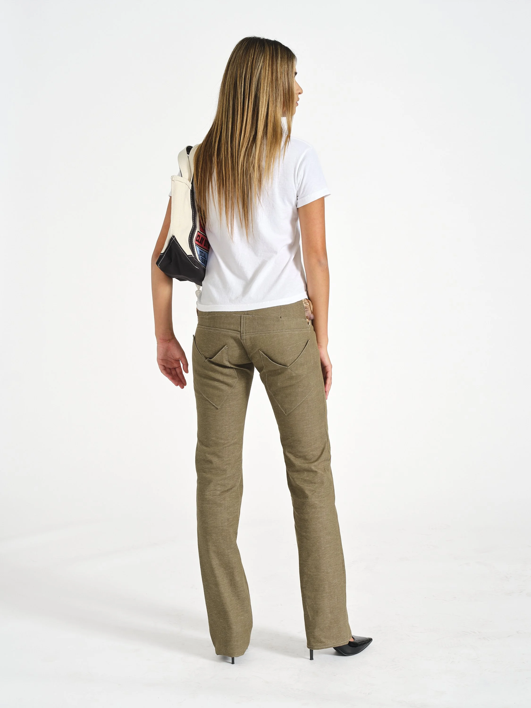 Woman in a white T-shirt and brown wide-leg pants carrying a tote bag, shown from the back against a white studio background