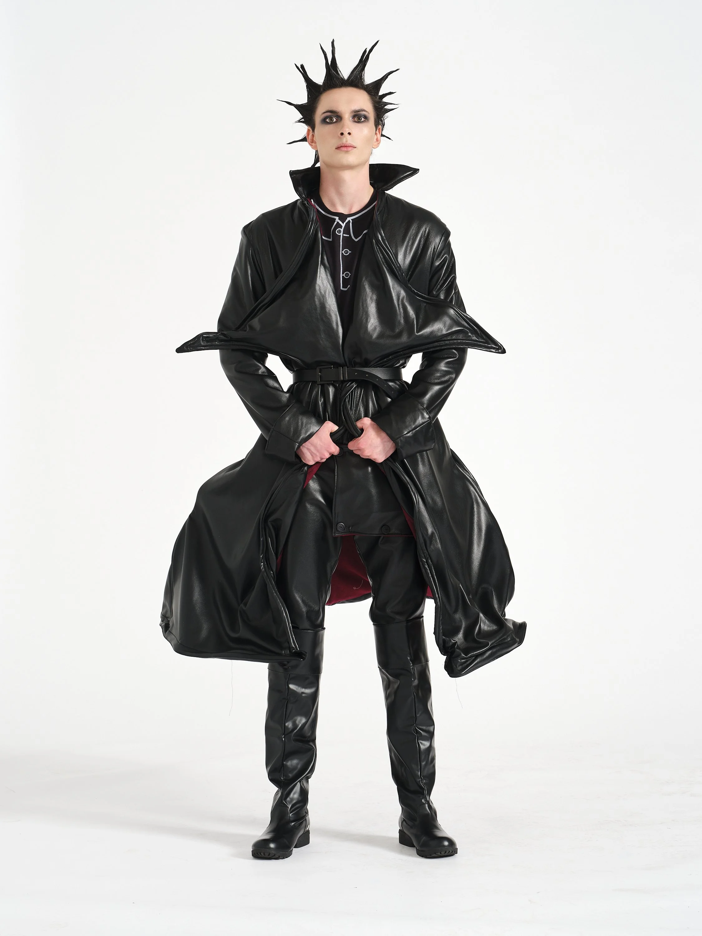 A male model dressed in a black, shiny, futuristic costume with spiked hairstyle posing against a plain white background.