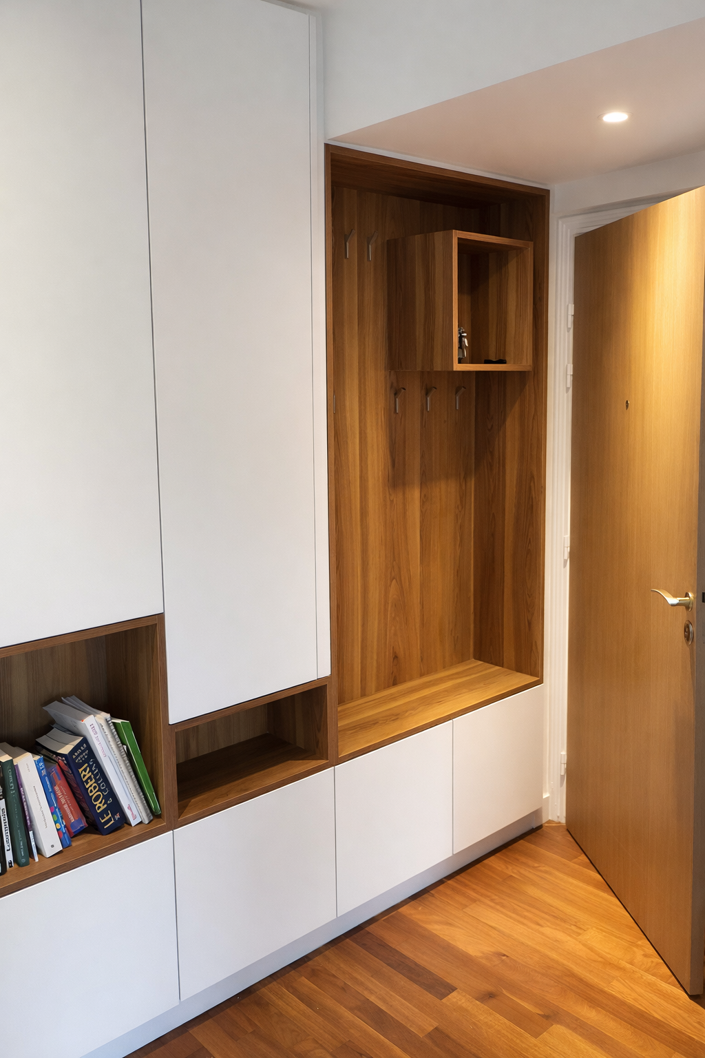 Entrée avec meuble en bois clair et blanc, étagère avec livres, et un panneau mural avec des crochets, porte en bois fermée.