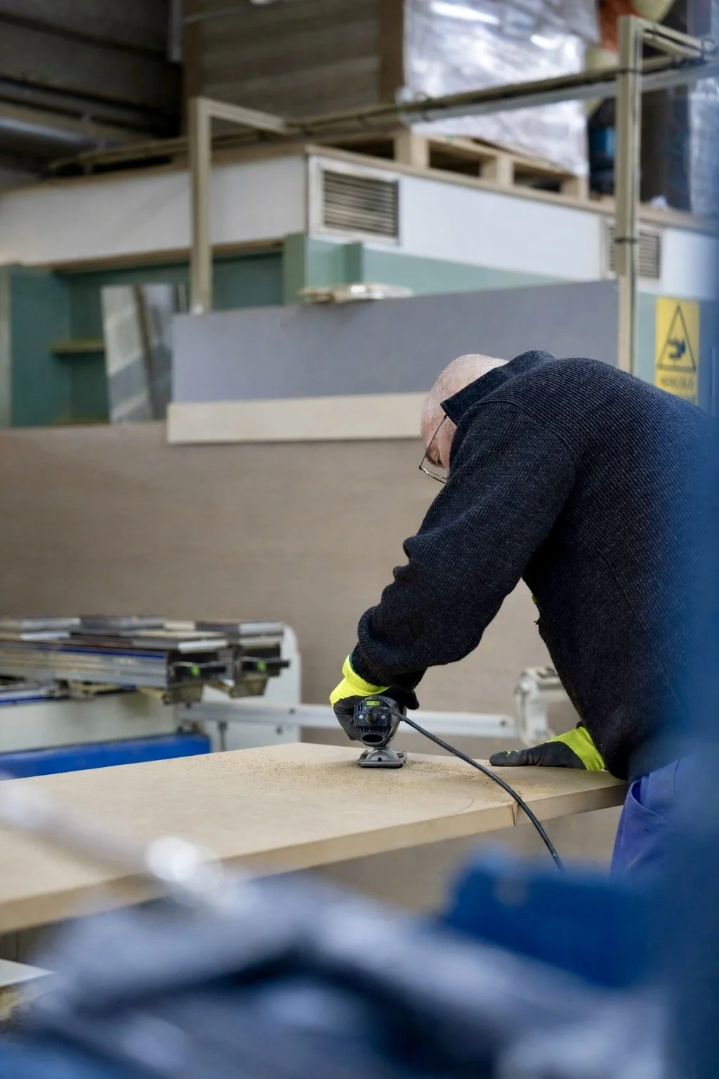 Un homme travaillant dans un atelier de menuiserie, utilisant une ponceuse sur une planche de bois.