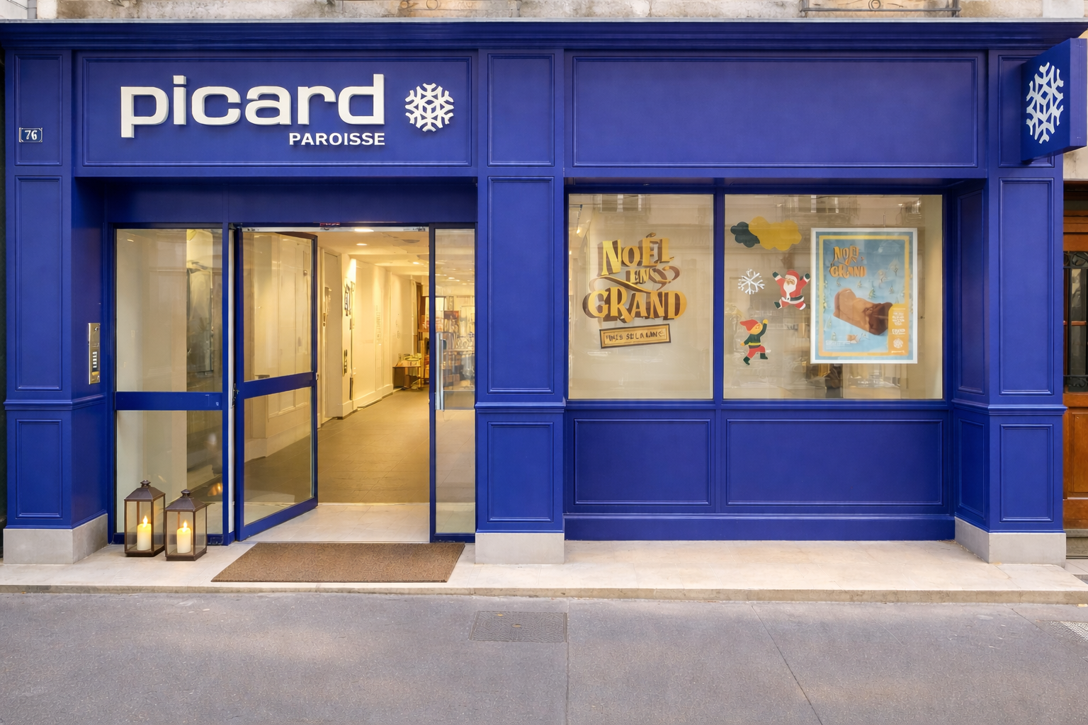 Façade d'une boutique appelée Picard Paroisse avec un mur bleu, deux lanternes avec des bougies à l'entrée, et des vitrines avec des décorations de Noël.