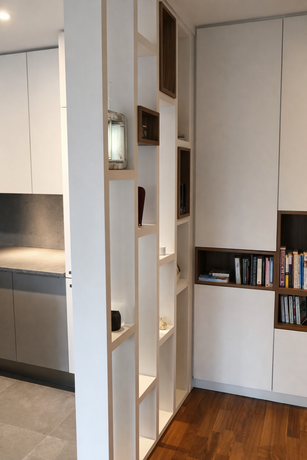 Etagère blanche avec plusieurs compartiments contenant des objets décoratifs, et mur avec bibliothèque en bois intégrée contenant des livres, dans un intérieur moderne.