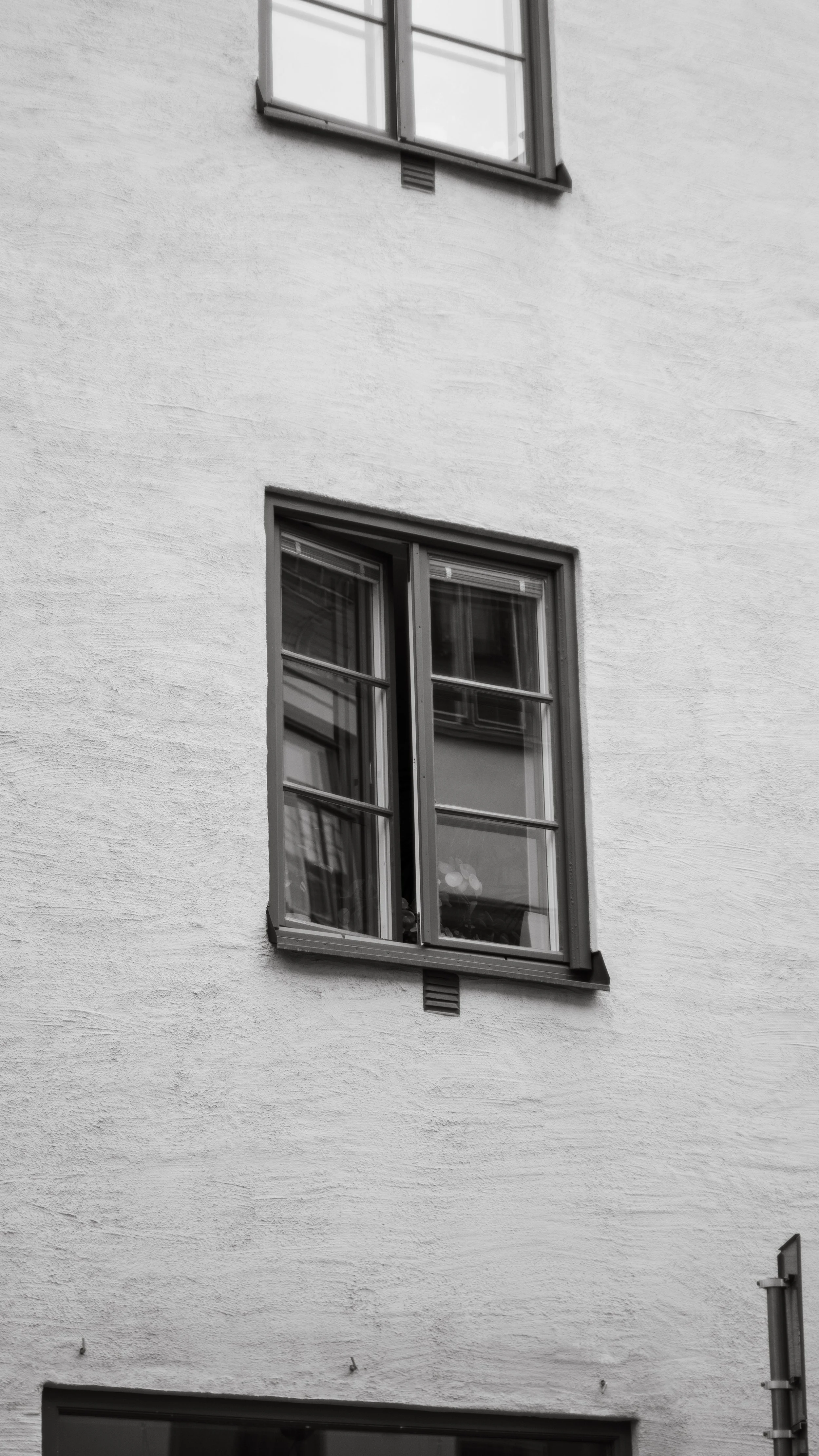 Black and white photo of a section of a building exterior showing two windows, one open and the other closed, with a textured wall surface.