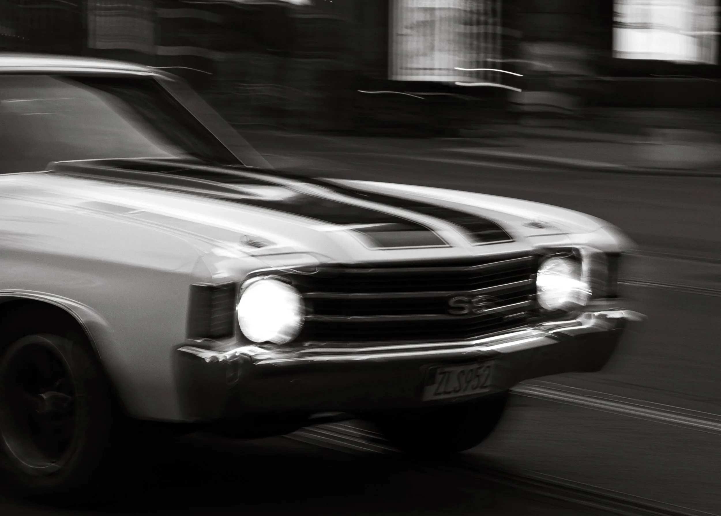 A black and white photo of a classic car driving on the street.