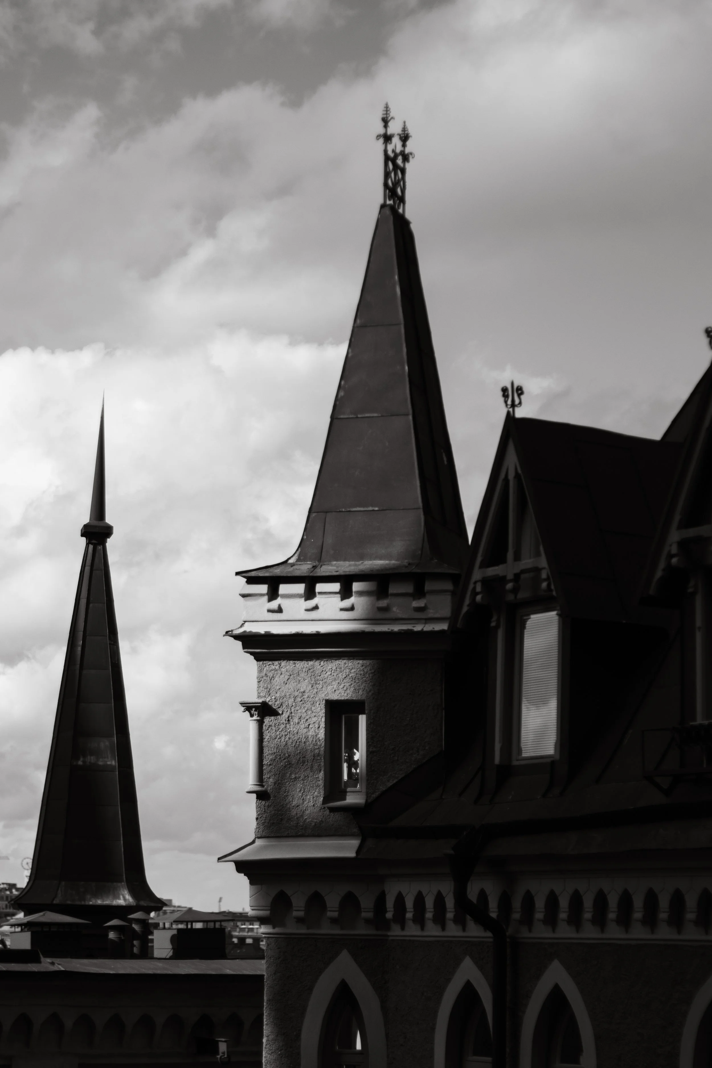 Black and white photo of pointed church steeples with intricate details and windows, against cloudy sky.